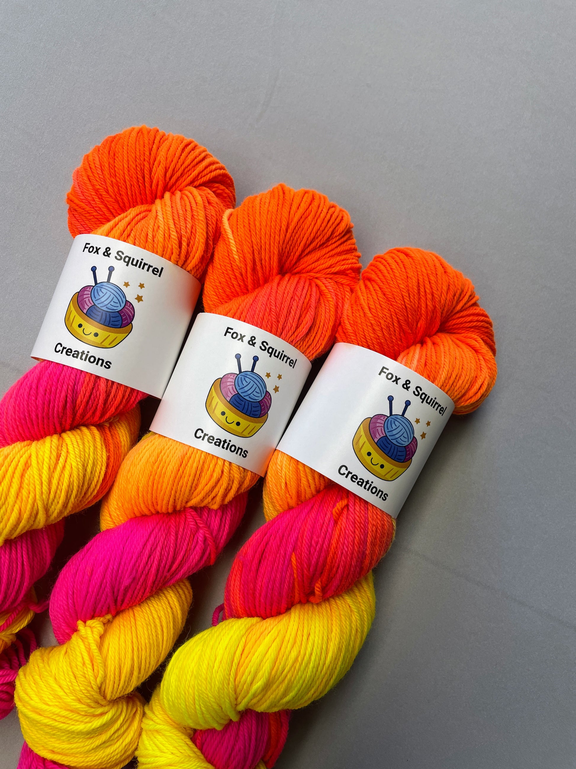 Close up shot of 100g DK weight yarn in colourway Neon Funk. This colourway has three bands of colour in Neon Yellow, Neon Pink and Neon Orange. Photographed on a light grey background.
