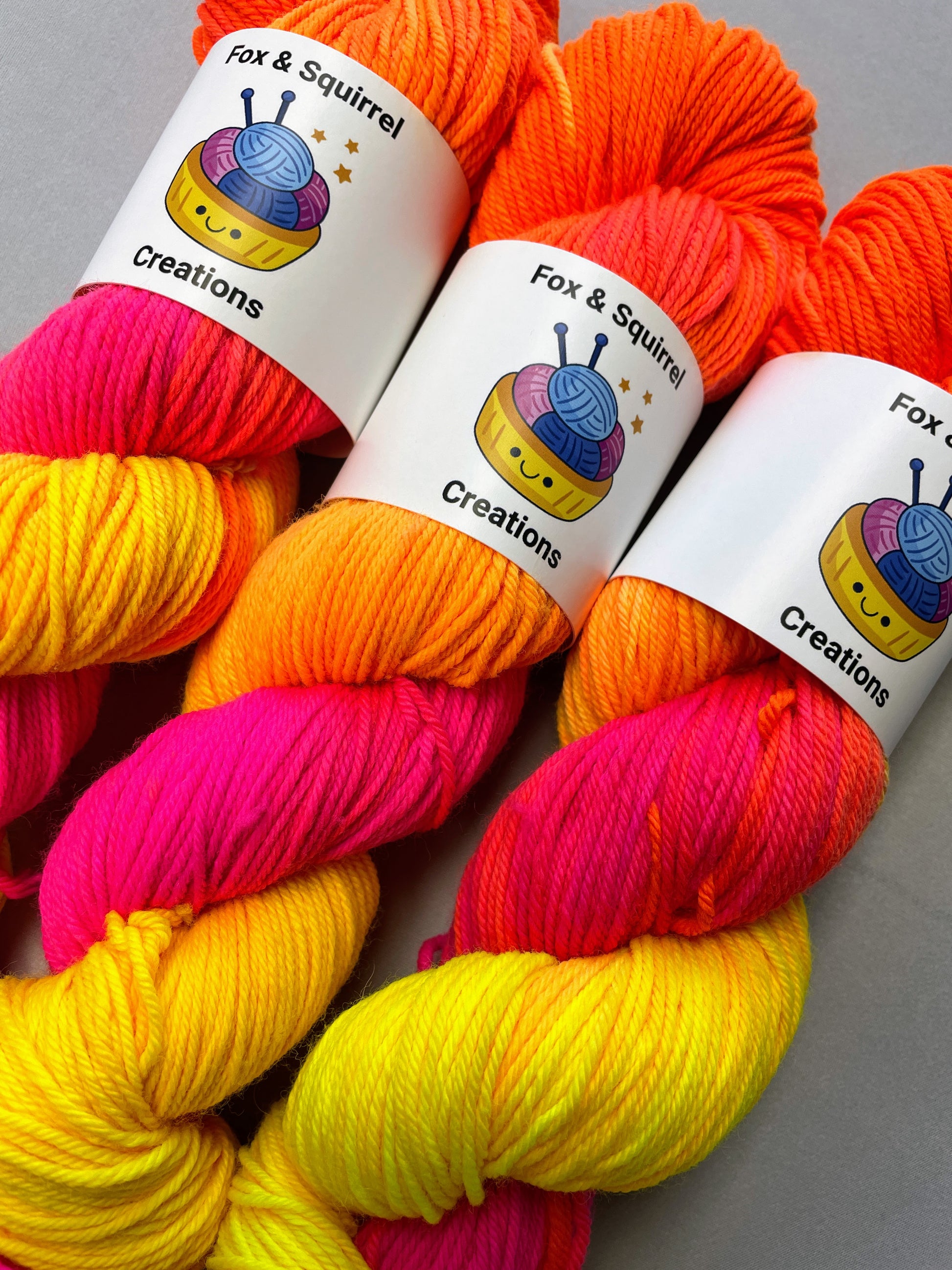 Close up shot of 100g DK weight yarn in colourway Neon Funk. This colourway has three bands of colour in Neon Yellow, Neon Pink and Neon Orange. Photographed on a light grey background.