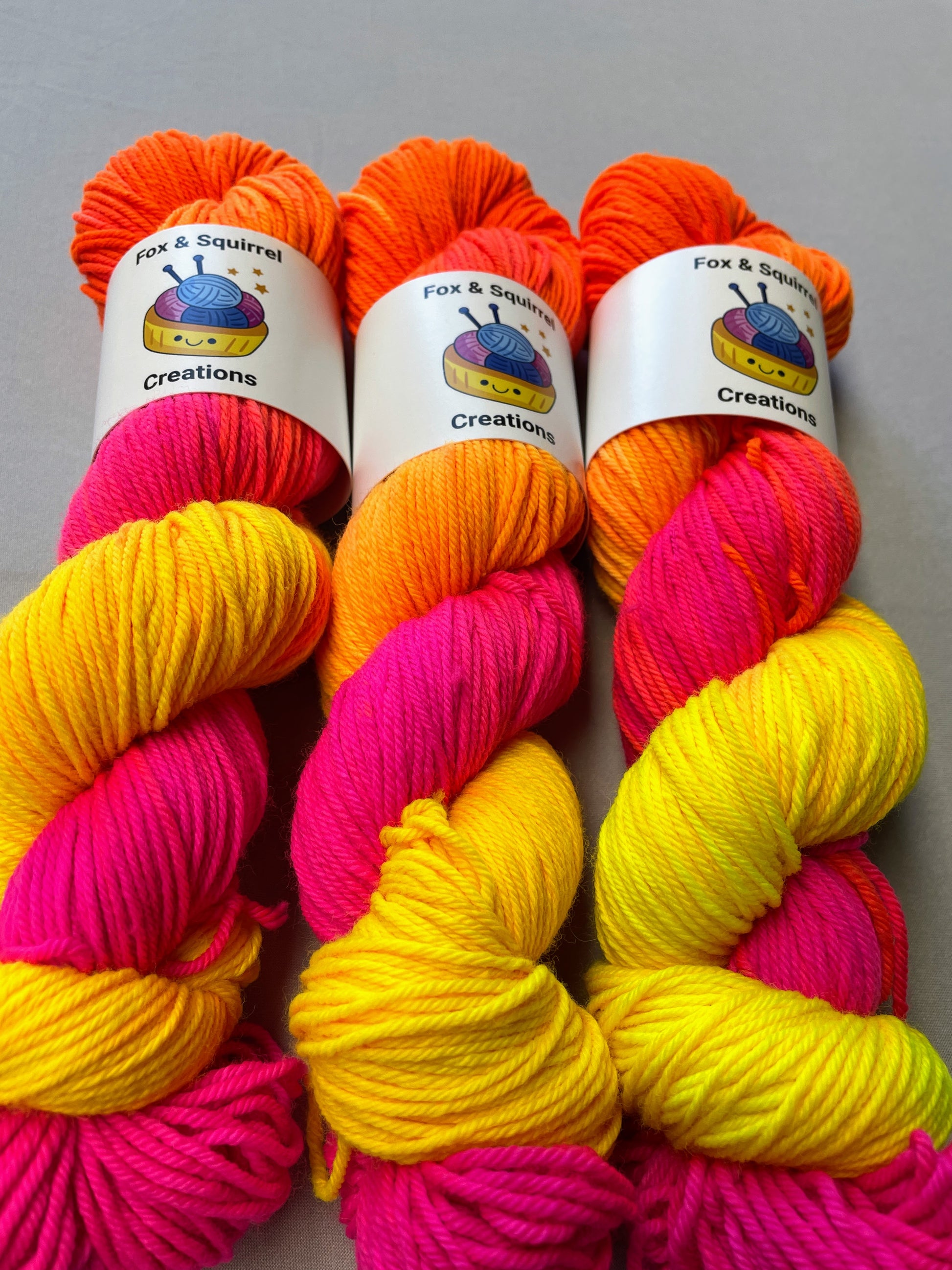 Close up shot of 100g DK weight yarn in colourway Neon Funk. This colourway has three bands of colour in Neon Yellow, Neon Pink and Neon Orange. Photographed on a light grey background.
