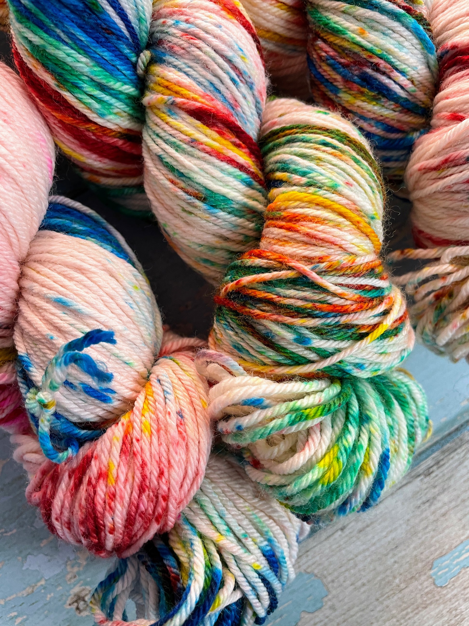 Close up shot of 100g DK weight yarn in colourway Rainbow Sprinkles. This is an undeyd yarn base with layers of speckles in red, yellow, green, blue. This image shows off the intensity of the speckles.