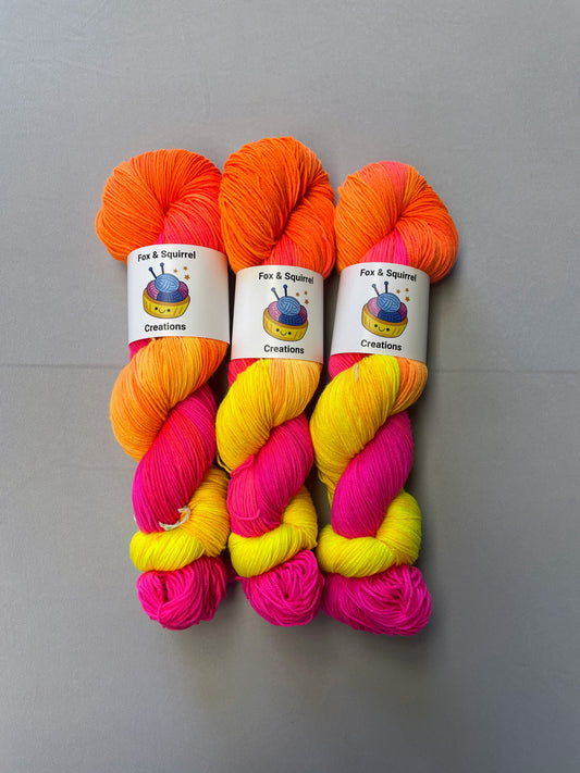 Full shot of 100g Sock weight yarn in colourway Neon Funk. This colourway has three bands of colour in Neon Yellow, Neon Pink and Neon Orange. Photographed on a light grey background.