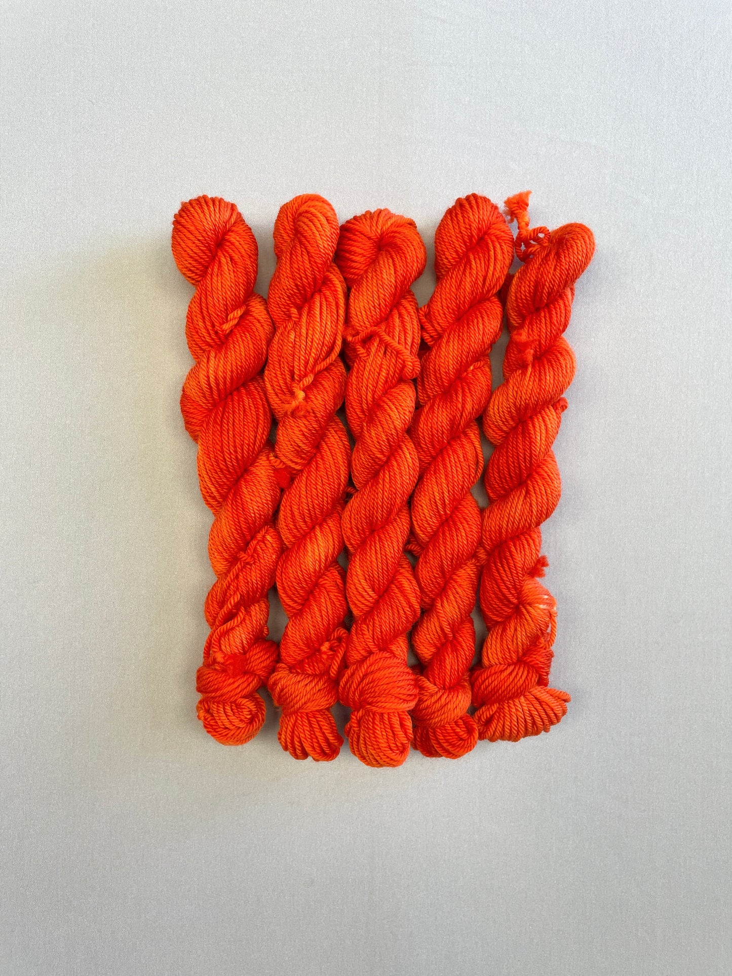 Full shot of DK weight mini skeins in colourway Lava. This semi-solid colourway is dyed up in a bright, intense orange.