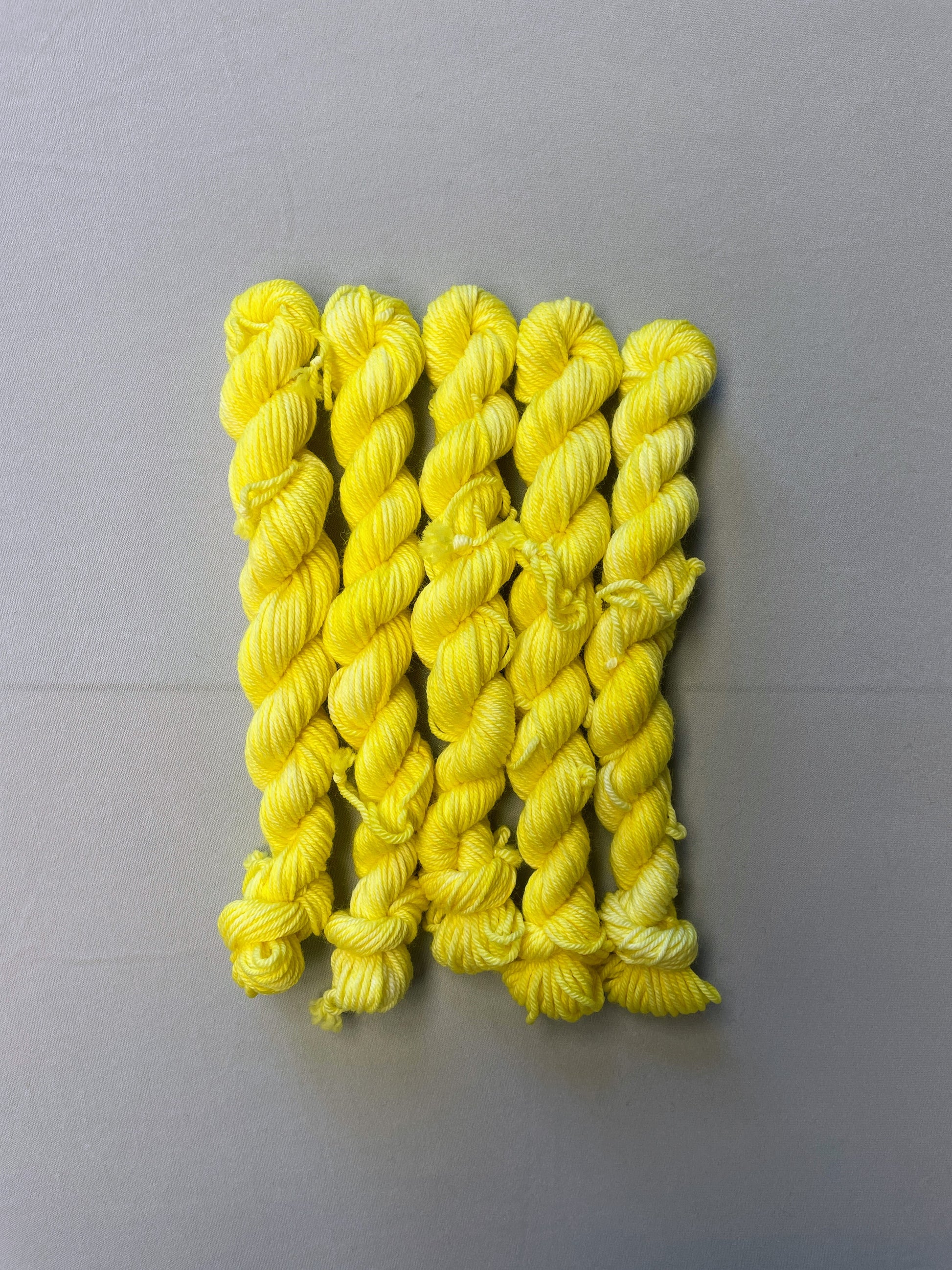 Full shot of 20g DK weight mini skeins in colourway Lemon. A semi-solid colourway of pale yellow colour.