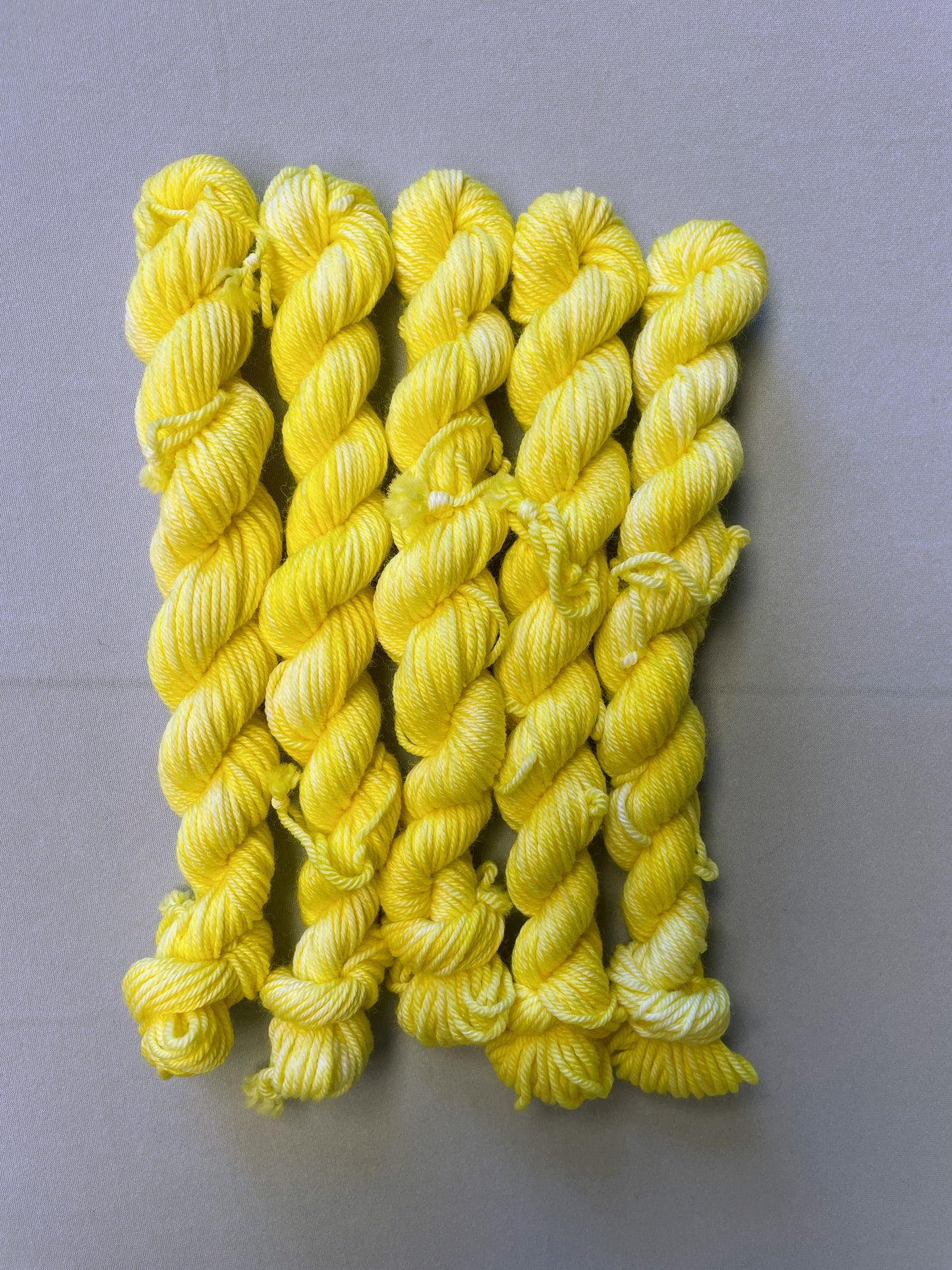 Zoomed in shot of 20g DK weight mini skeins in colourway Lemon. A semi-solid colourway of pale yellow colour.