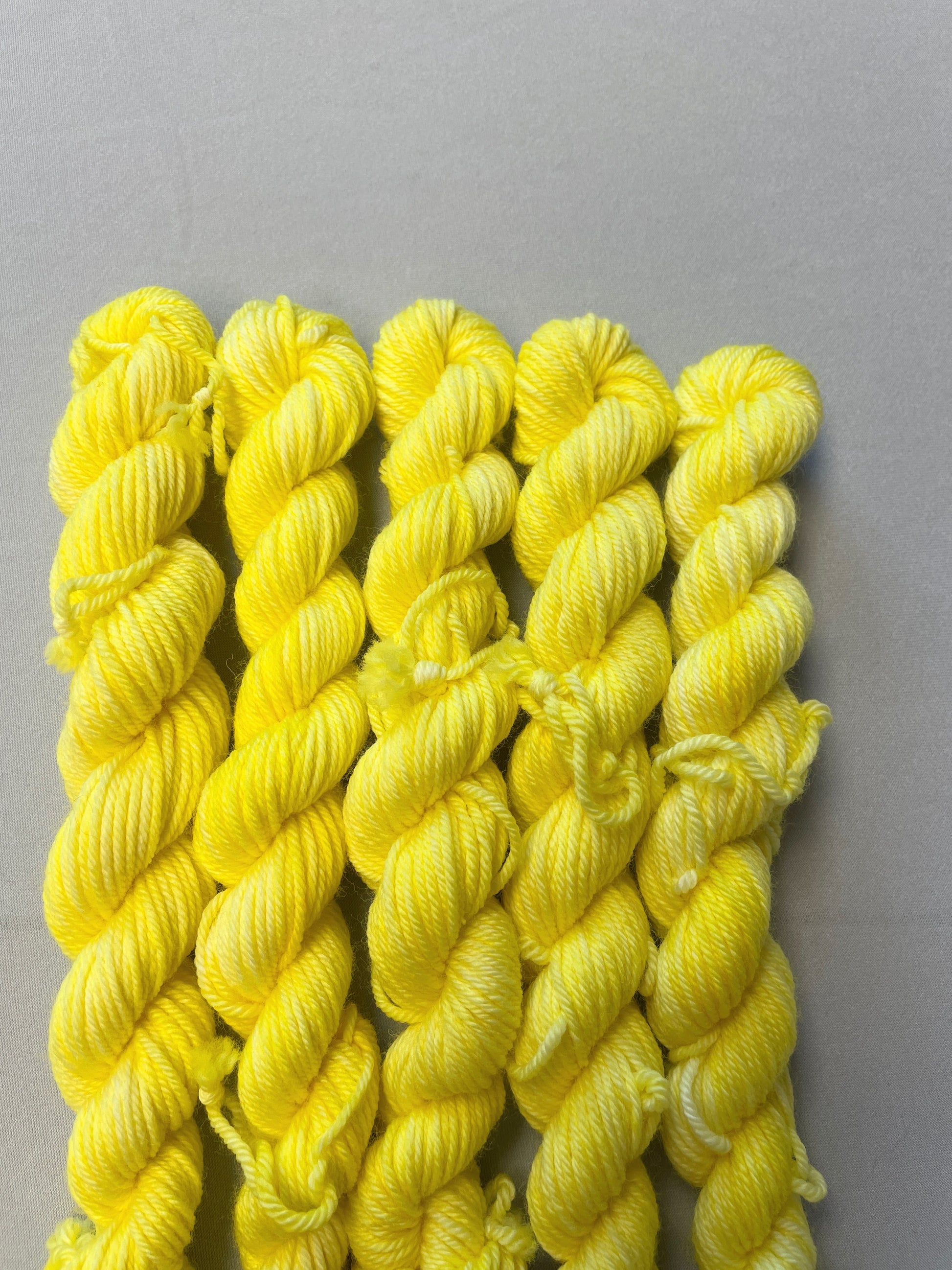 Close up shot 20g DK weight mini skeins in colourway Lemon. A semi-solid colourway of pale yellow colour.