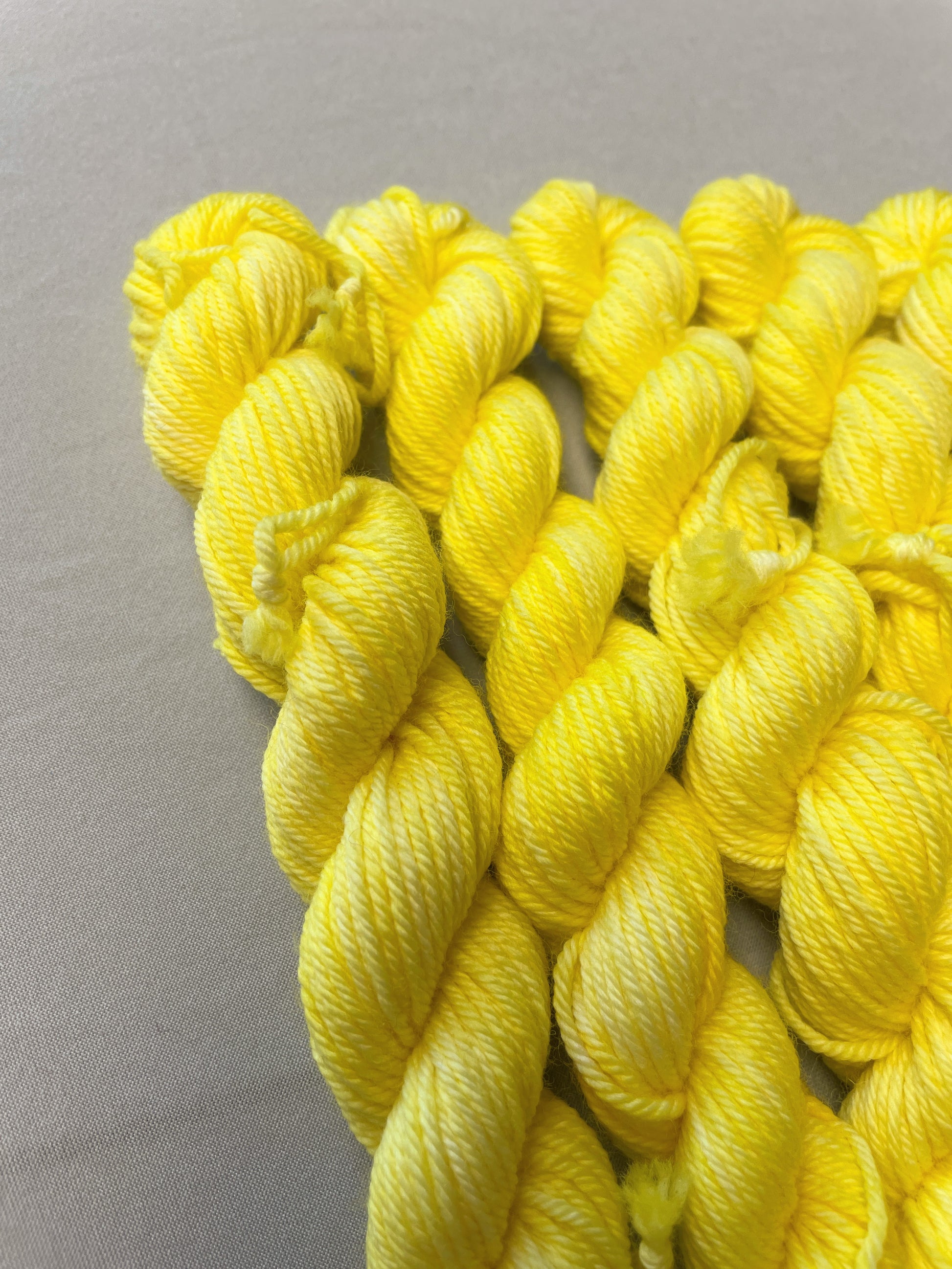 Close up shot 20g DK weight mini skeins in colourway Lemon. A semi-solid colourway of pale yellow colour.