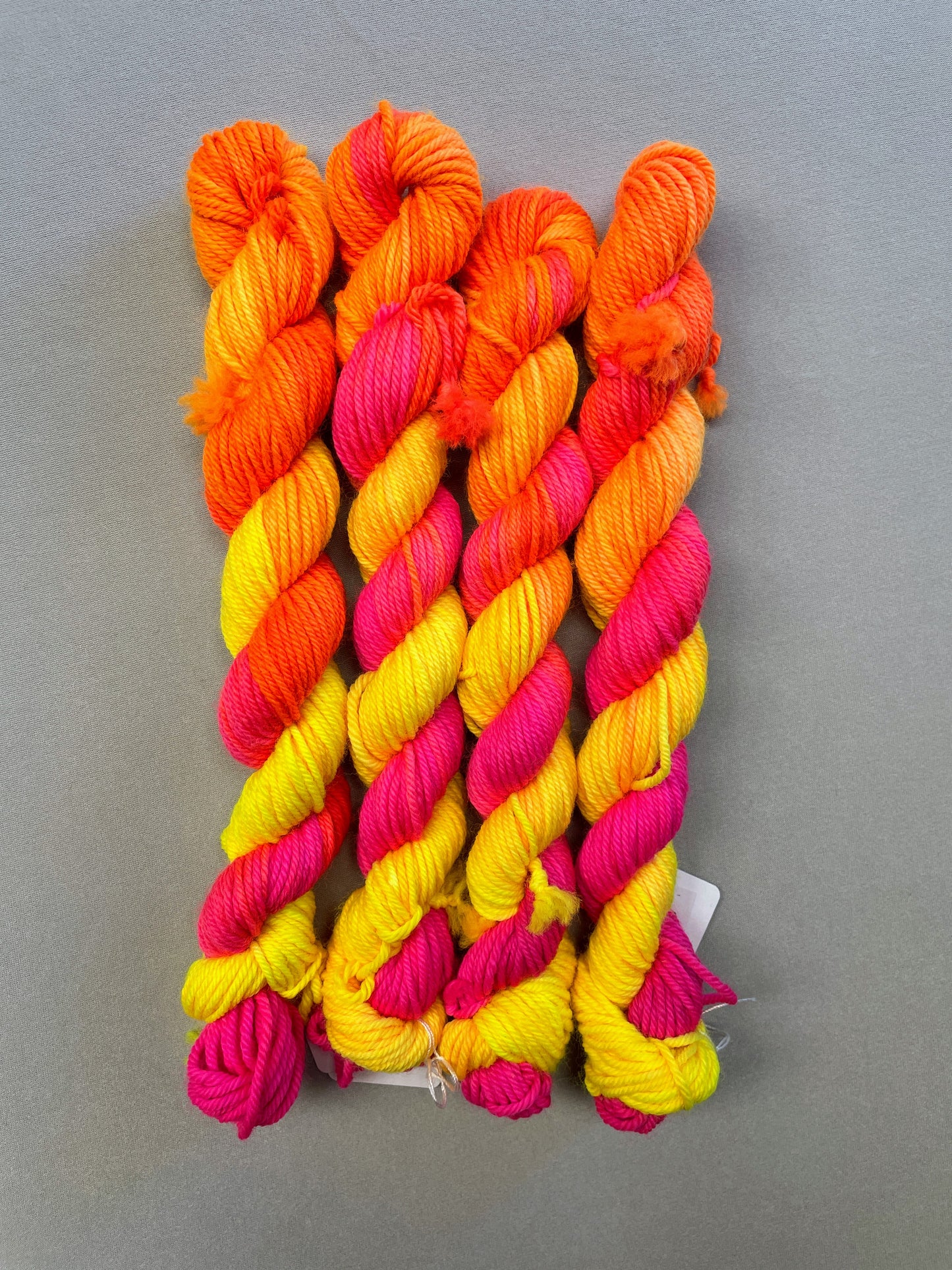 Full shot of 20g DK mini skeins in colourway Neon Funk. This colourway has three bands of colour in Neon Yellow, Neon Pink and Neon Orange. Photographed on a light grey background.