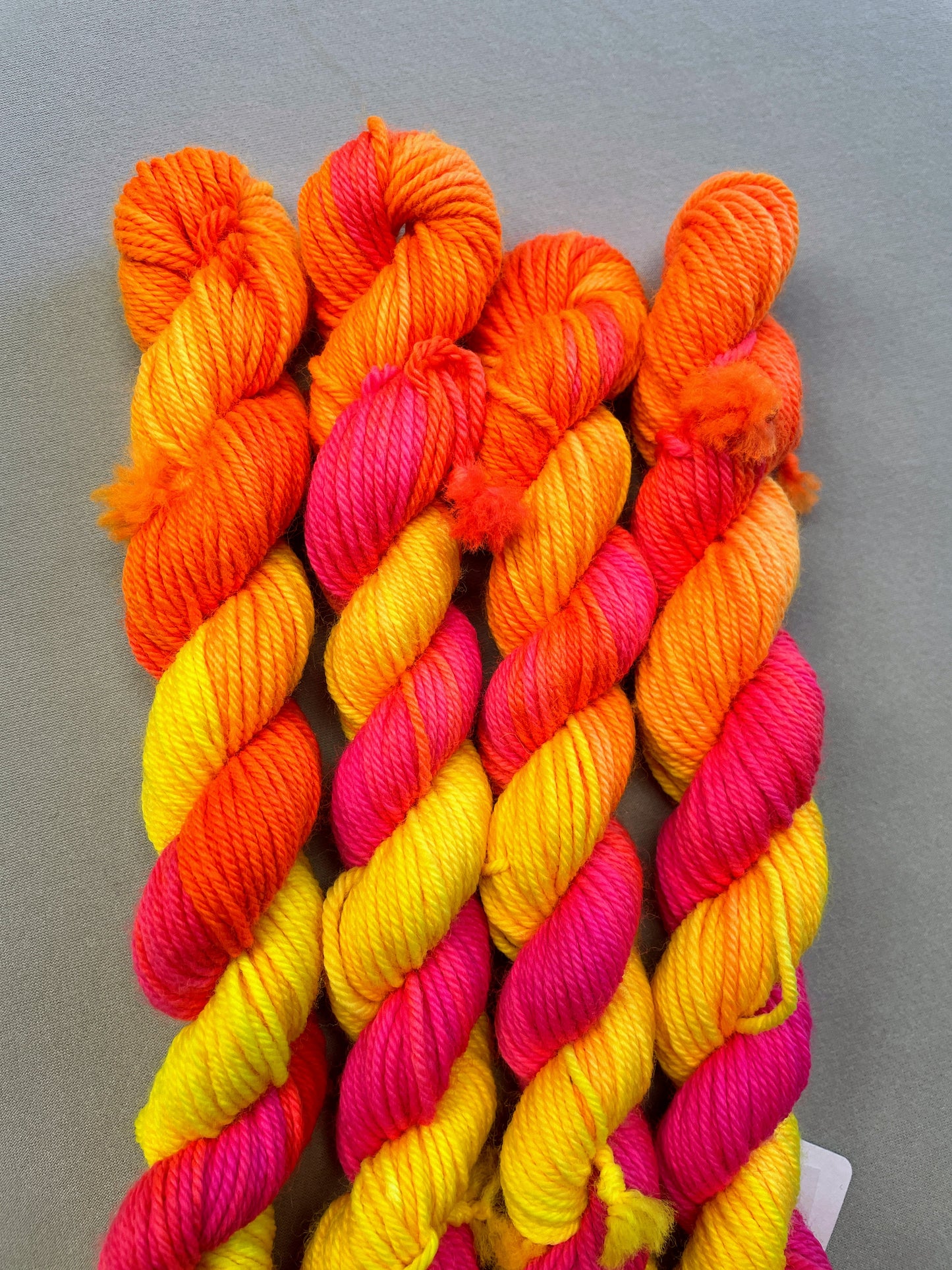 Zoomed in shot of 20g DK mini skeins in colourway Neon Funk. This colourway has three bands of colour in Neon Yellow, Neon Pink and Neon Orange. Photographed on a light grey background.