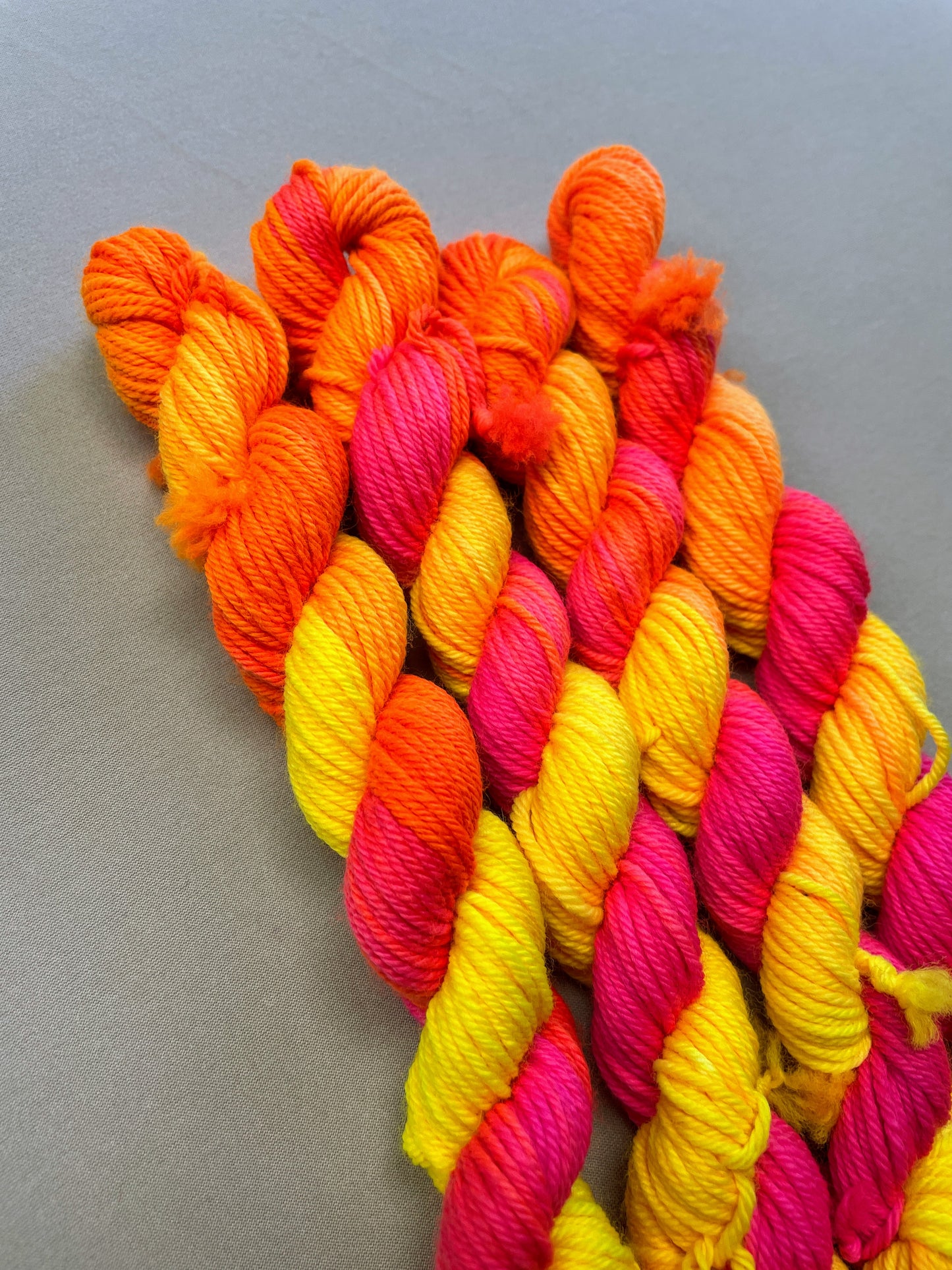 Close up shot of 20g DK mini skeins in colourway Neon Funk. This colourway has three bands of colour in Neon Yellow, Neon Pink and Neon Orange. Photographed on a light grey background.