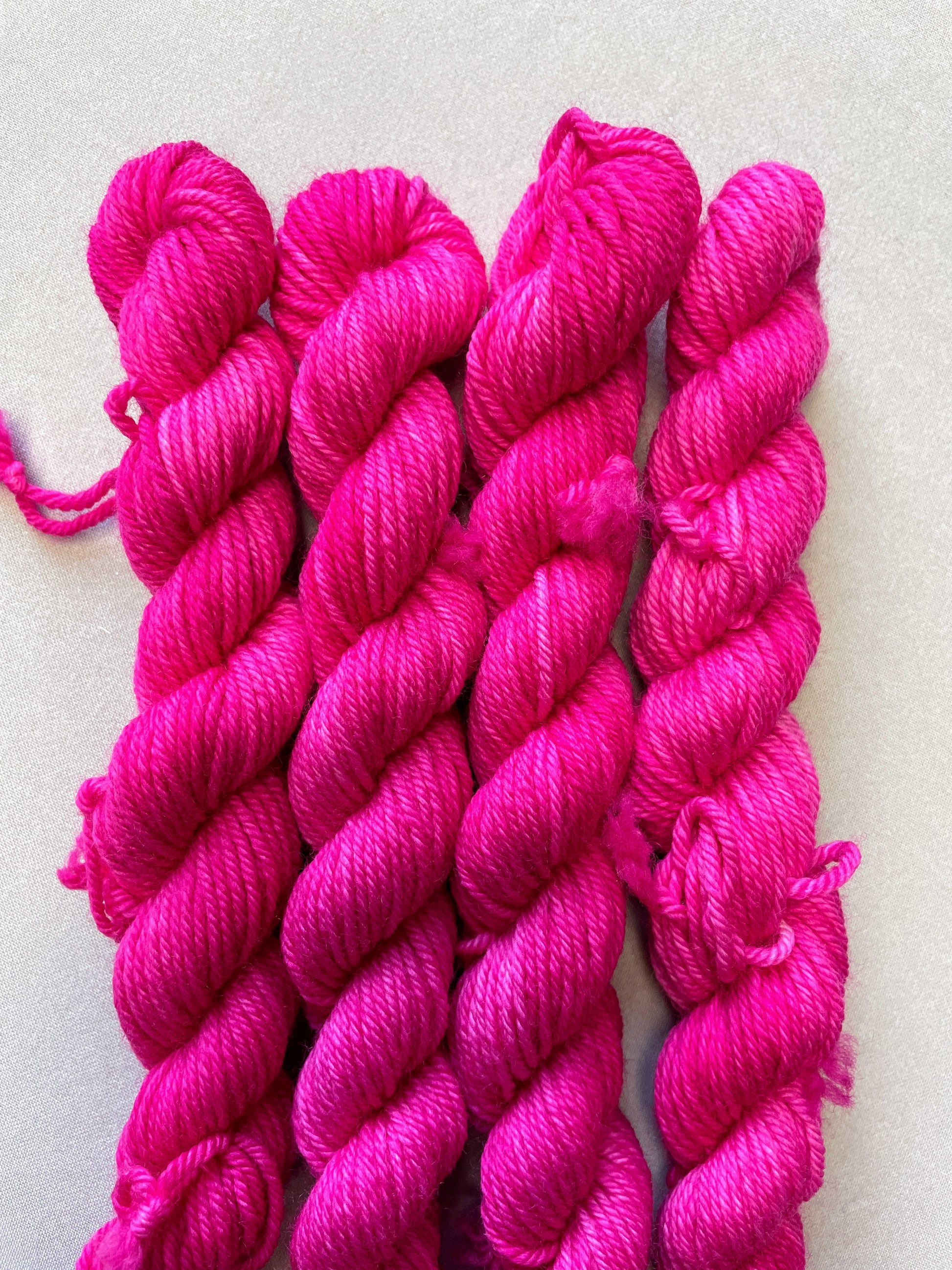 Close up shot of 20g DK weight mini skeins in colourway Pink. A semi-solid colourway in a bright pink shade.
