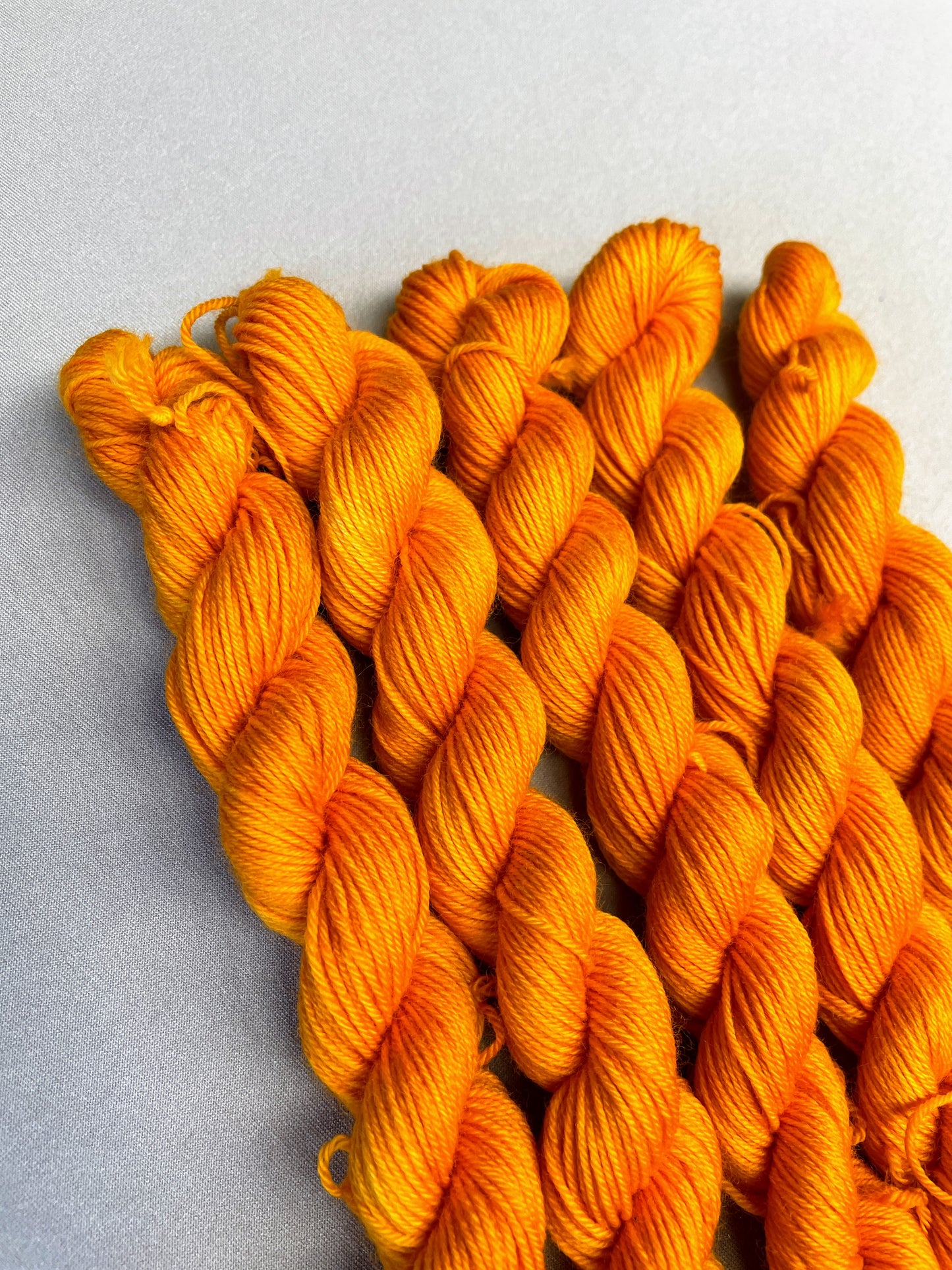 5 x 20g twisted, Sock mini skeins in colourway Golden Poppy, photographed on light grey background. Golden Poppy is a semi-solid colourway in a golden, yellow tone.