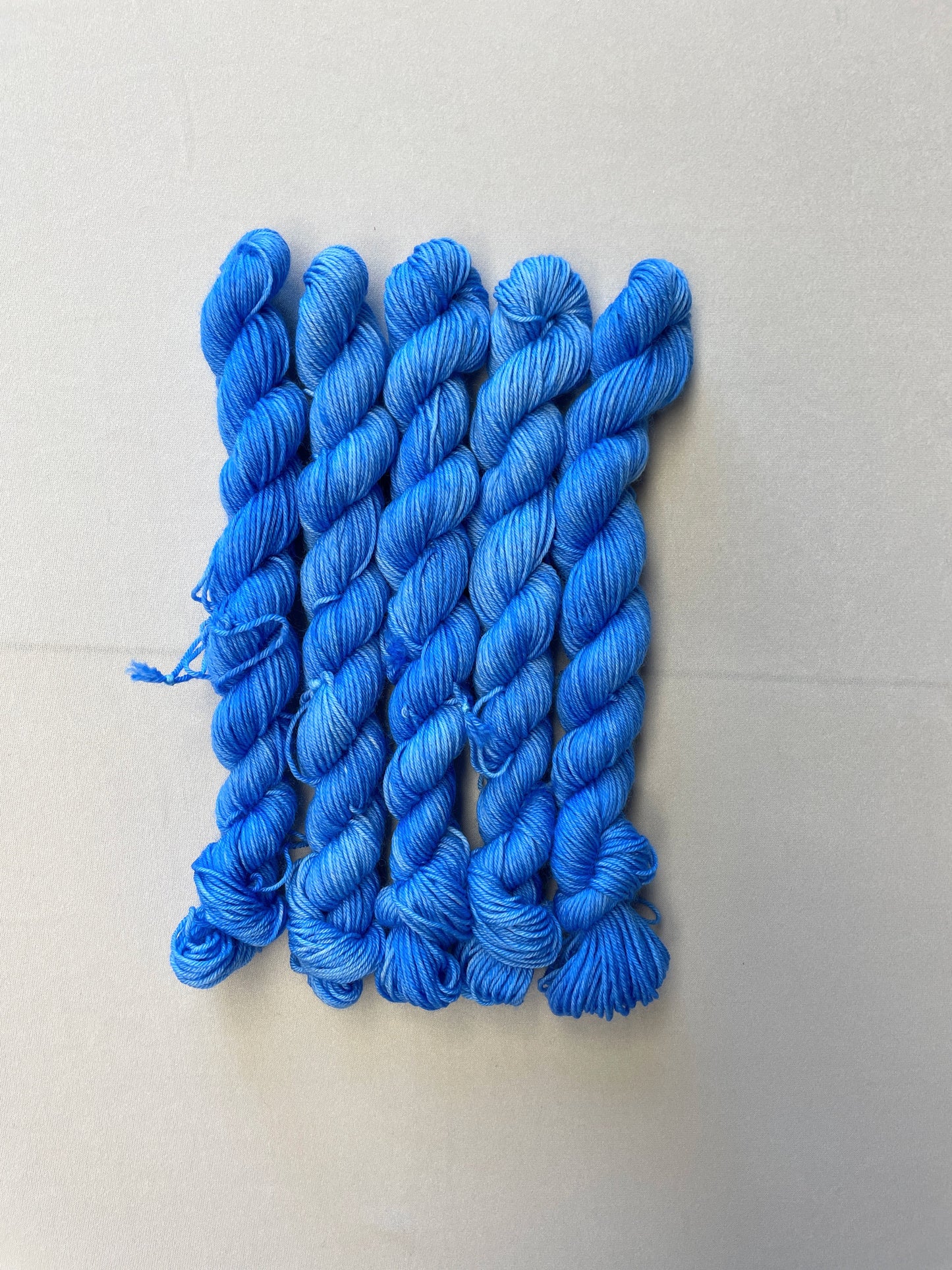 Full shot of 20g sock weight mini skeins in the semi-solid colourway Intense Blue. This colourway is a light blue colour.