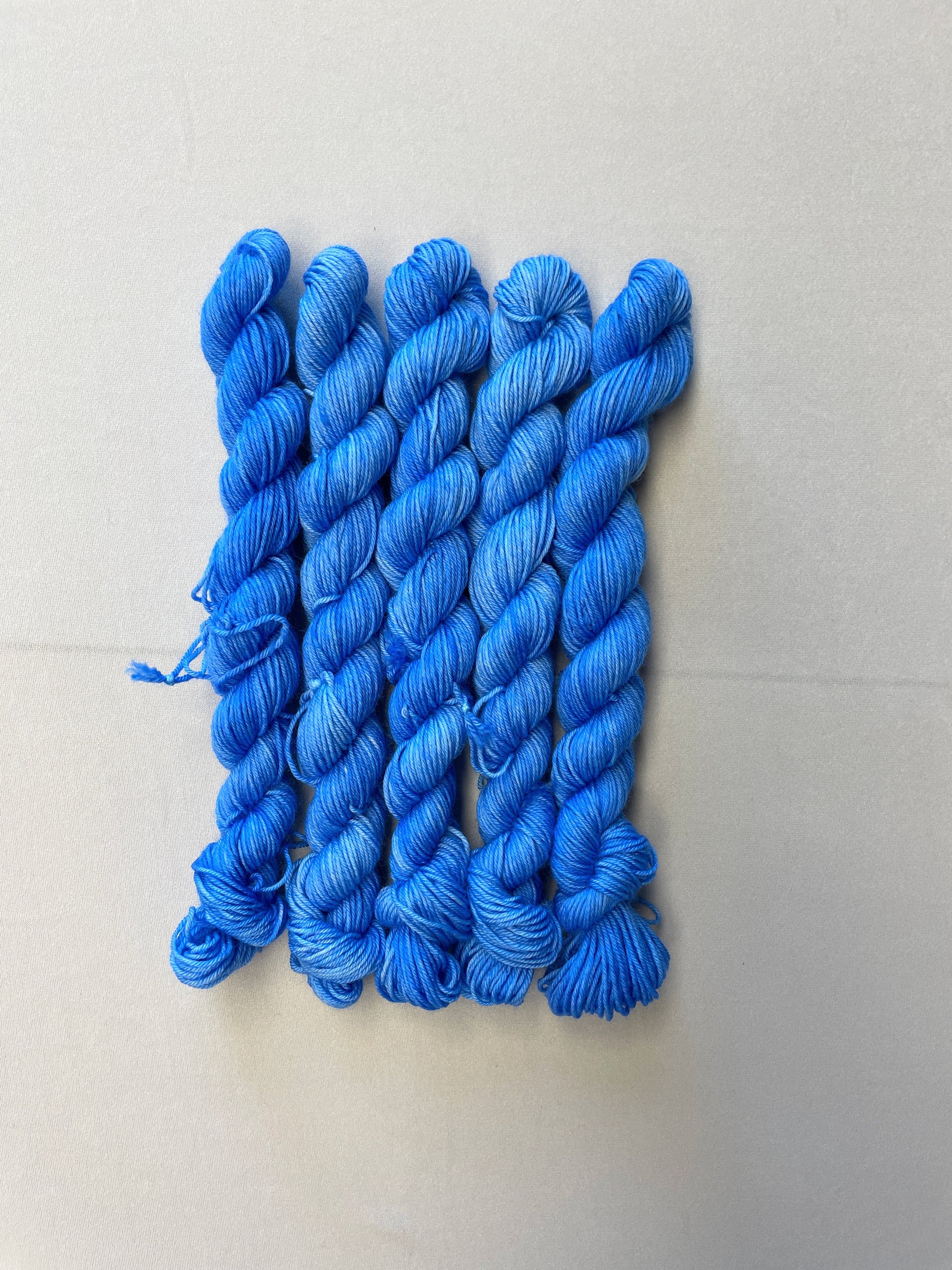 Full shot of 20g sock weight mini skeins in the semi-solid colourway Intense Blue. This colourway is a light blue colour.