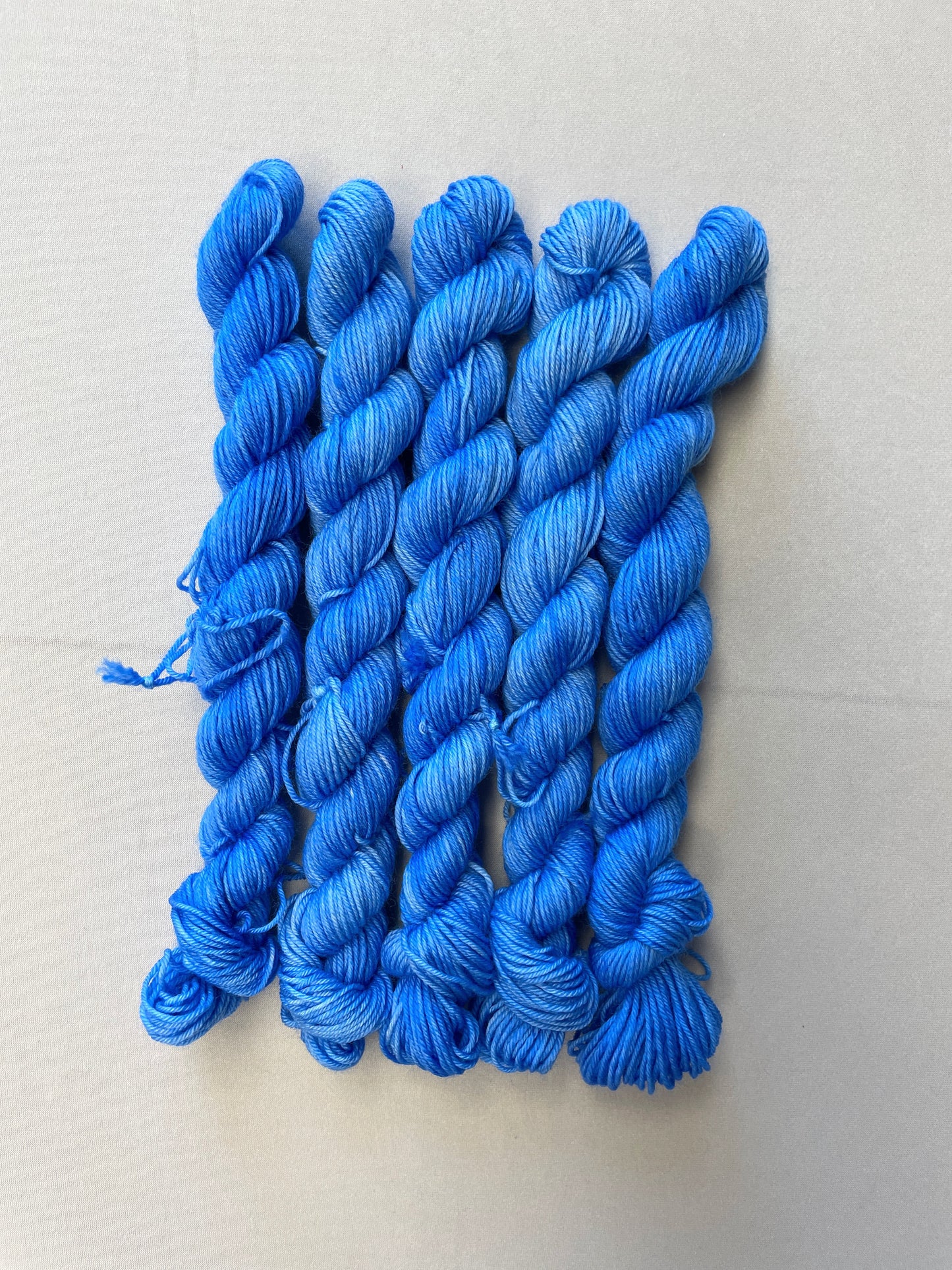 Zoomed in shot of 20g sock weight mini skeins in the semi-solid colourway Intense Blue. This colourway is a light blue colour.