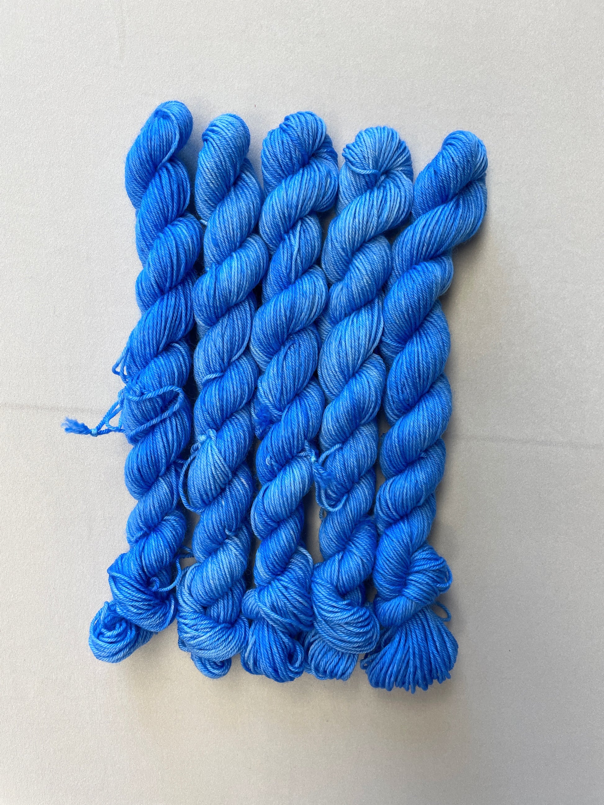 Zoomed in shot of 20g sock weight mini skeins in the semi-solid colourway Intense Blue. This colourway is a light blue colour.