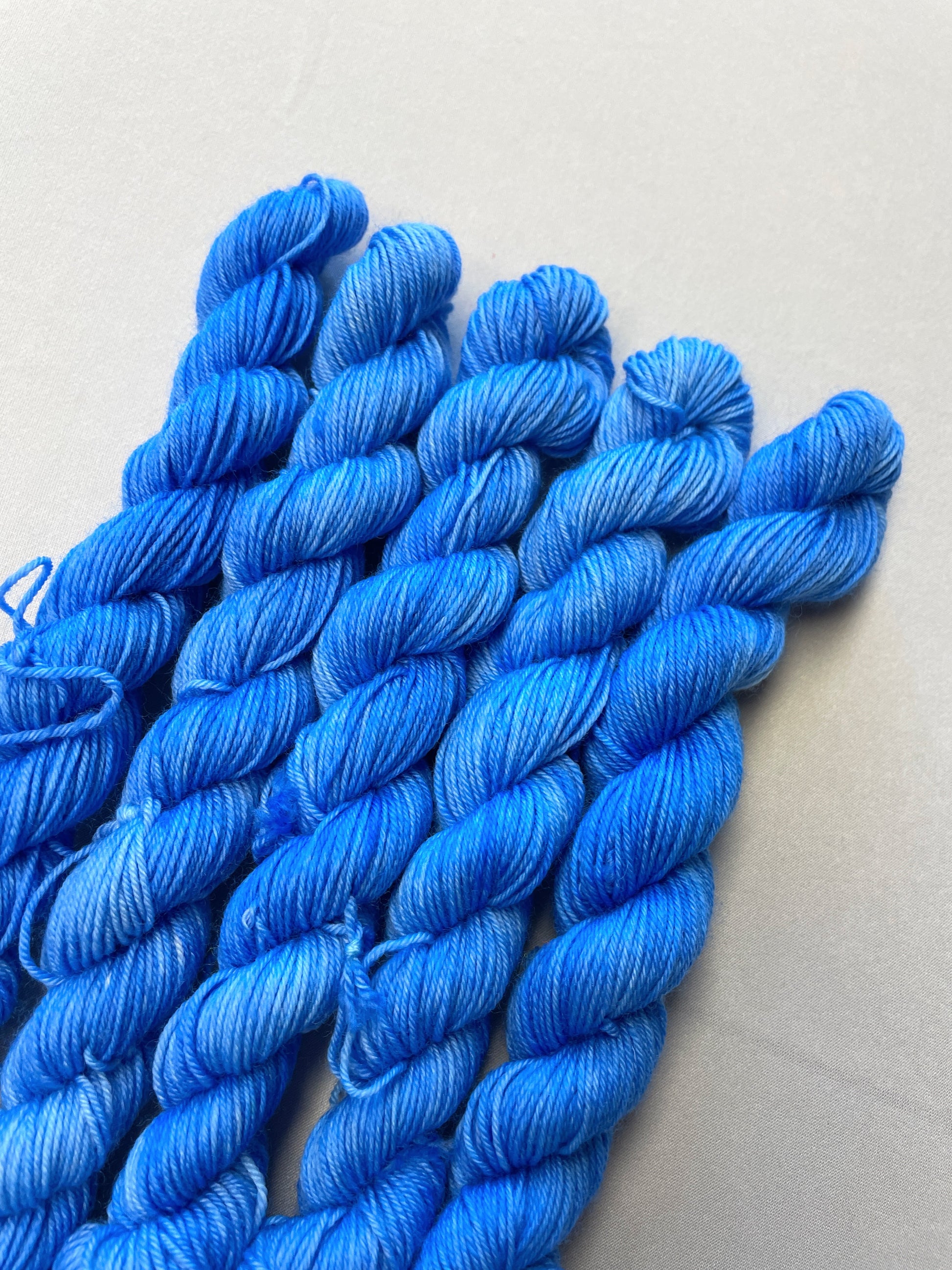 Close up shot of 20g sock weight mini skeins in the semi-solid colourway Intense Blue. This colourway is a light blue colour.