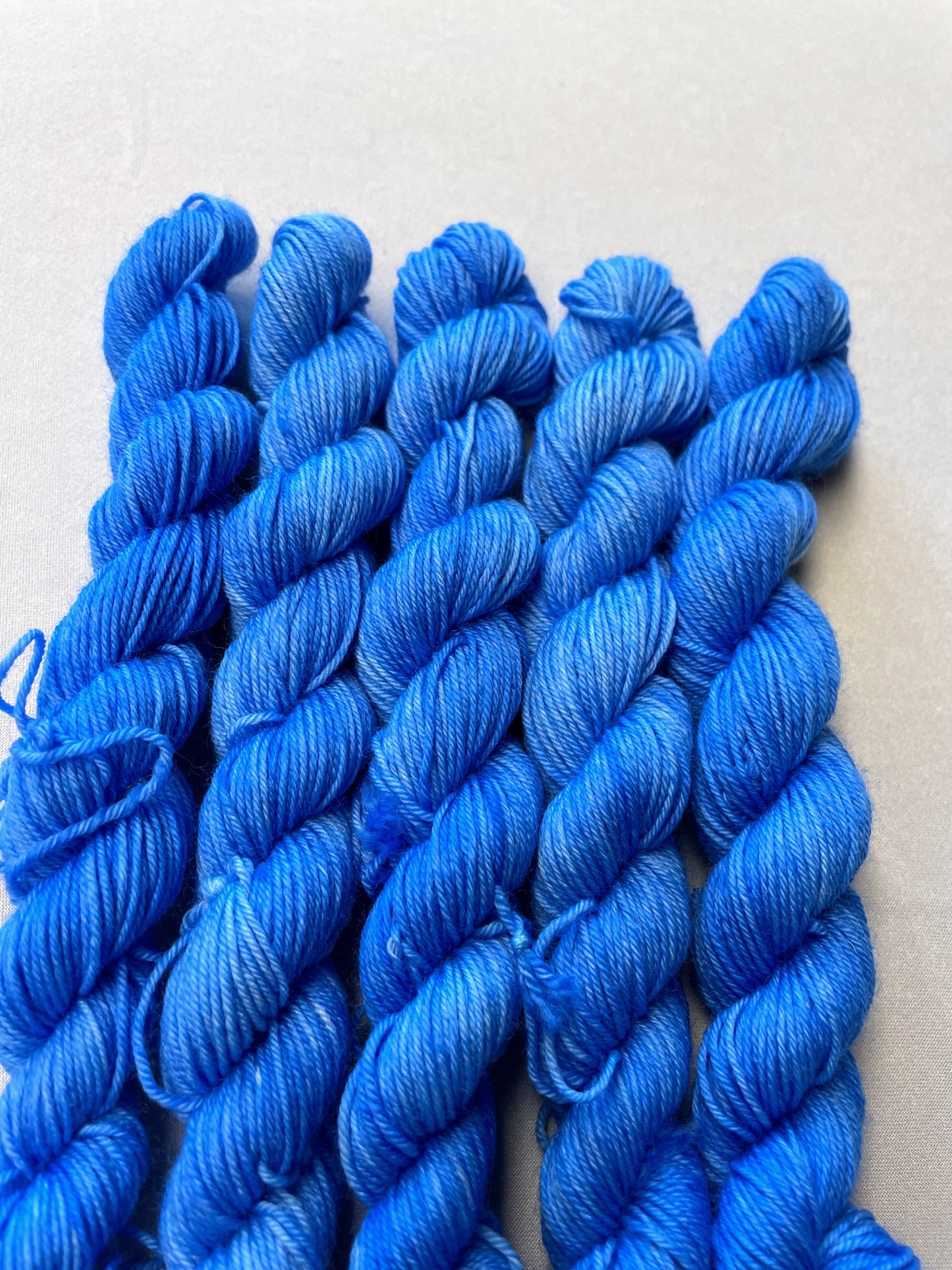 Close up shot of 20g sock weight mini skeins in the semi-solid colourway Intense Blue. This colourway is a light blue colour.