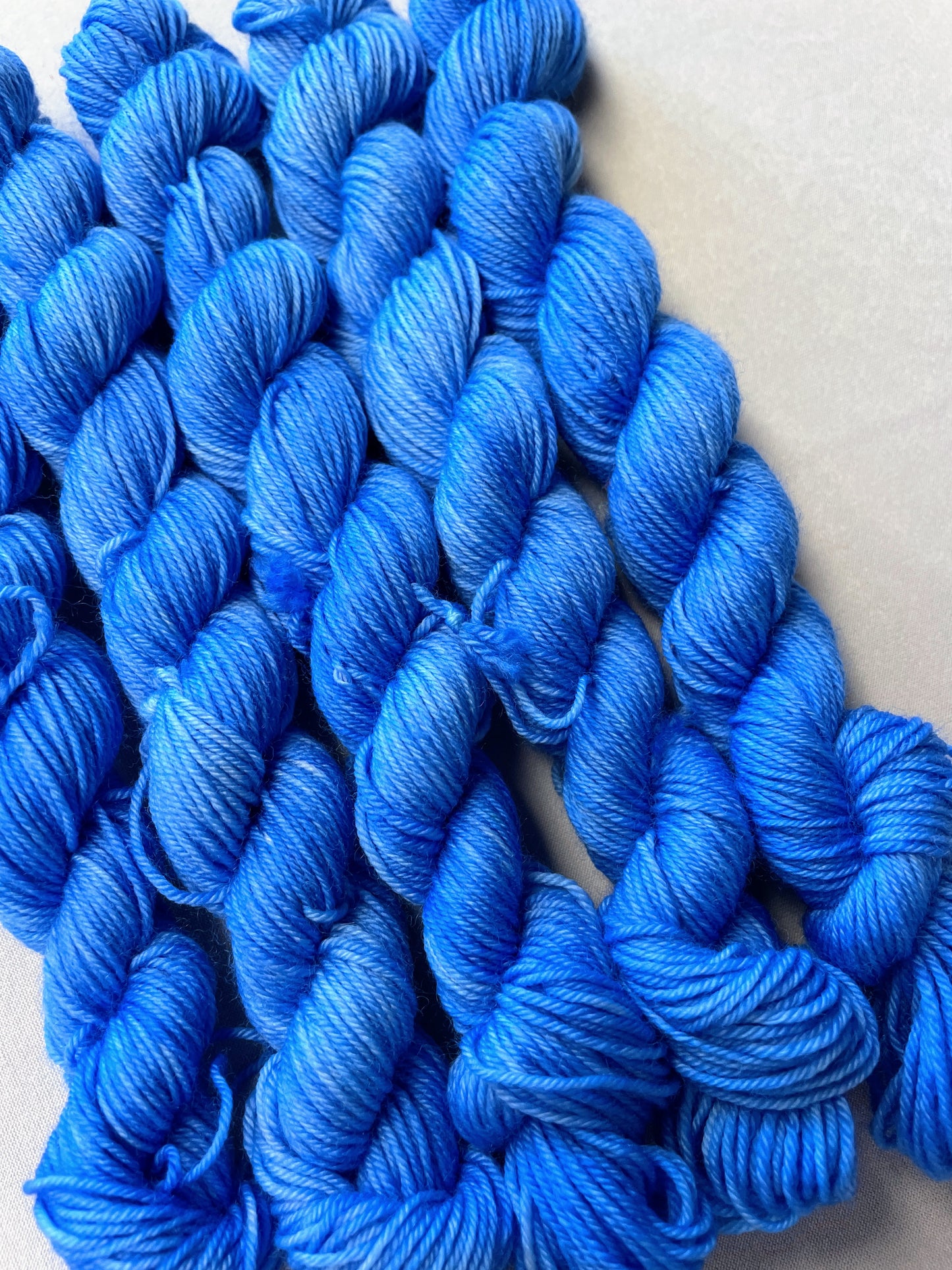 Angled shot of 20g sock weight mini skeins in the semi-solid colourway Intense Blue. This colourway is a light blue colour.
