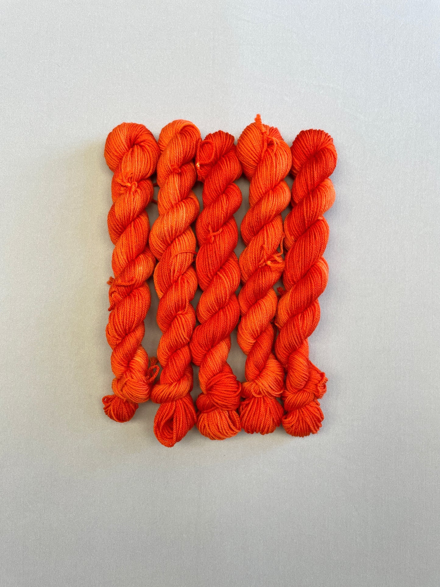 Full shot of Sock weight mini skeins in colourway Lava. This semi-solid colourway is dyed up in a bright, intense orange.