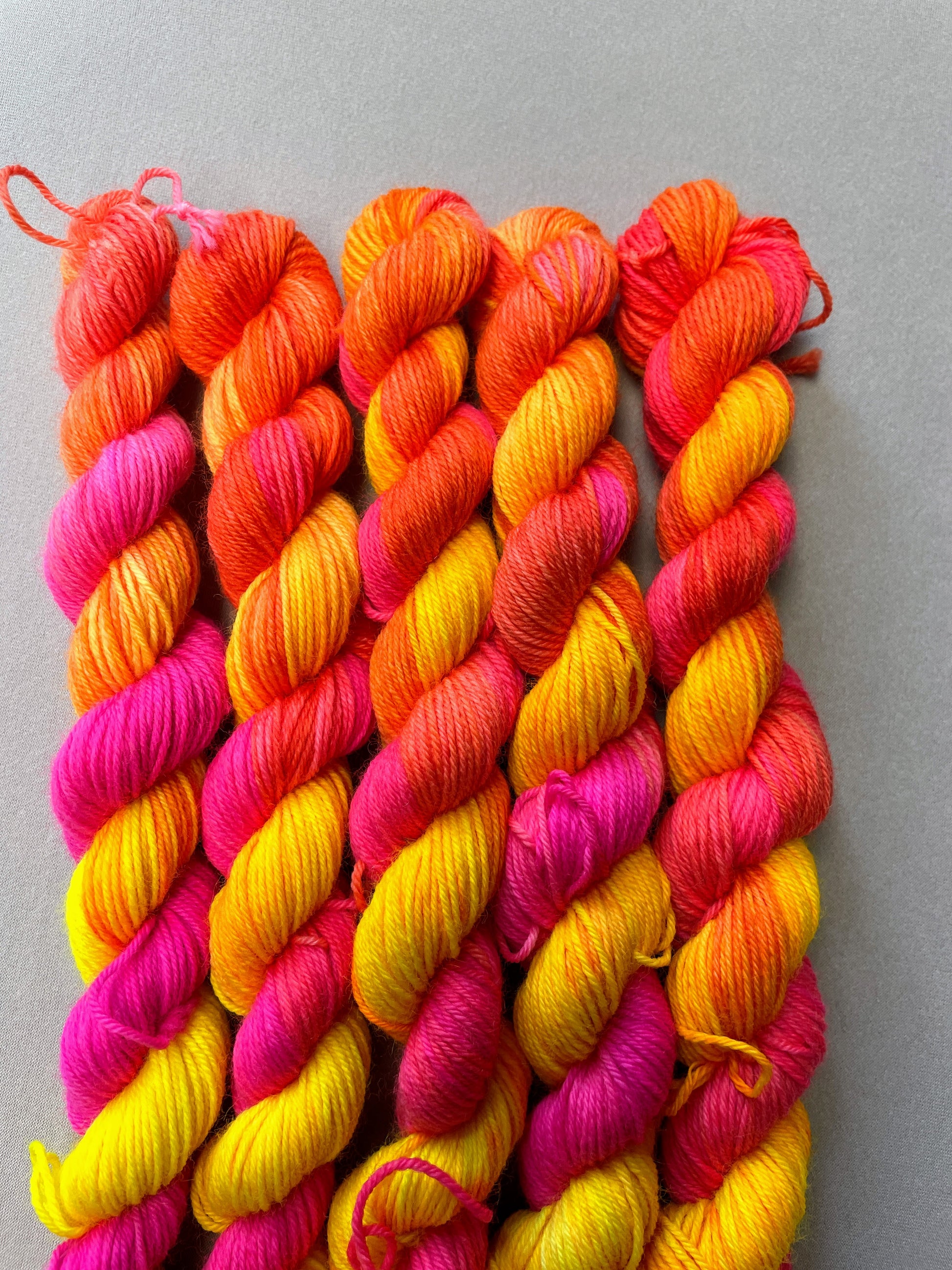Zoomed in shot of 20g sock mini skeins in colourway Neon Funk. This colourway has three bands of colour in Neon Yellow, Neon Pink and Neon Orange. Photographed on a light grey background.