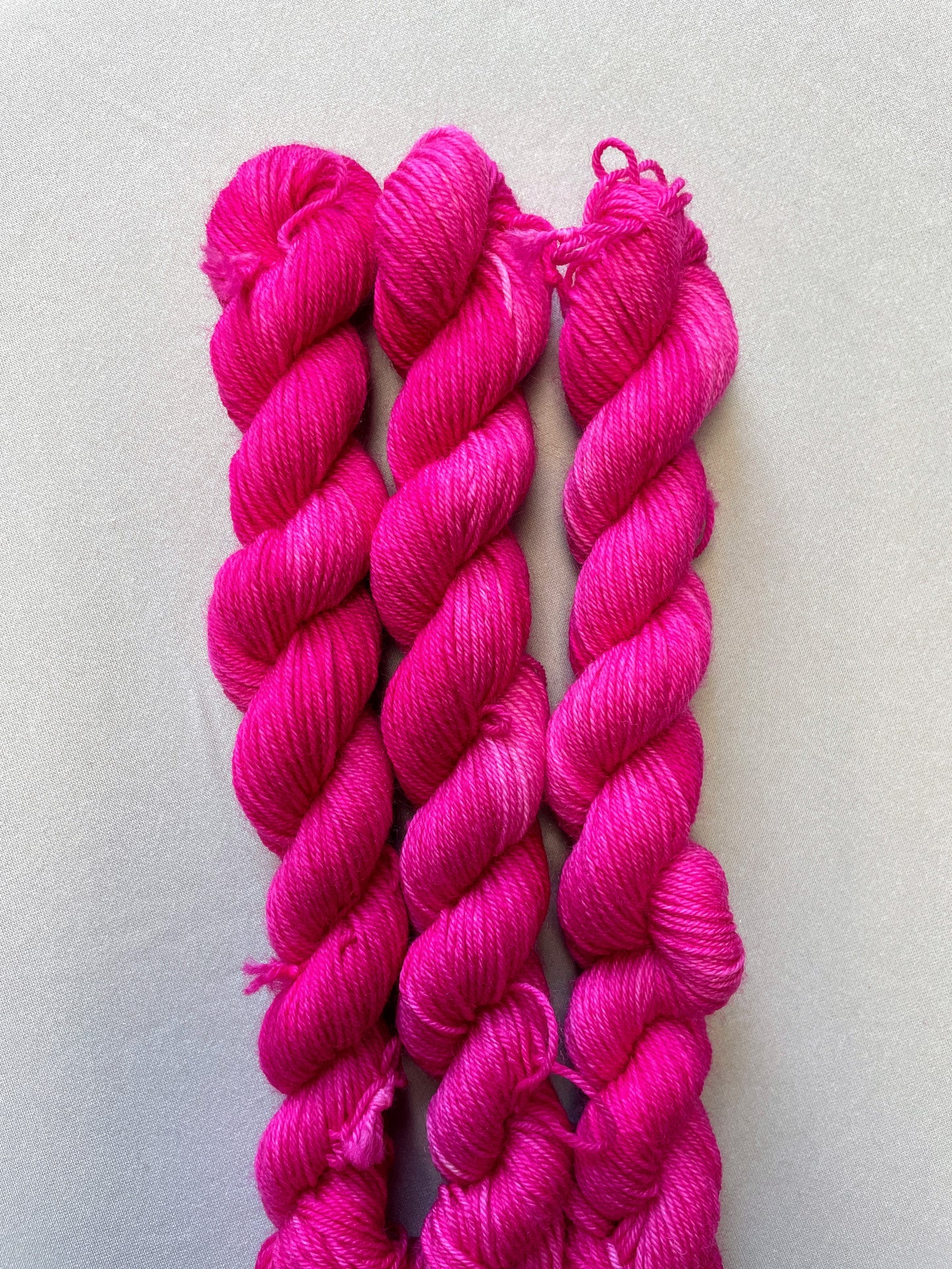 Close up shot of 20g sock weight mini skeins in colourway Pink. A semi-solid colourway in a bright pink shade.