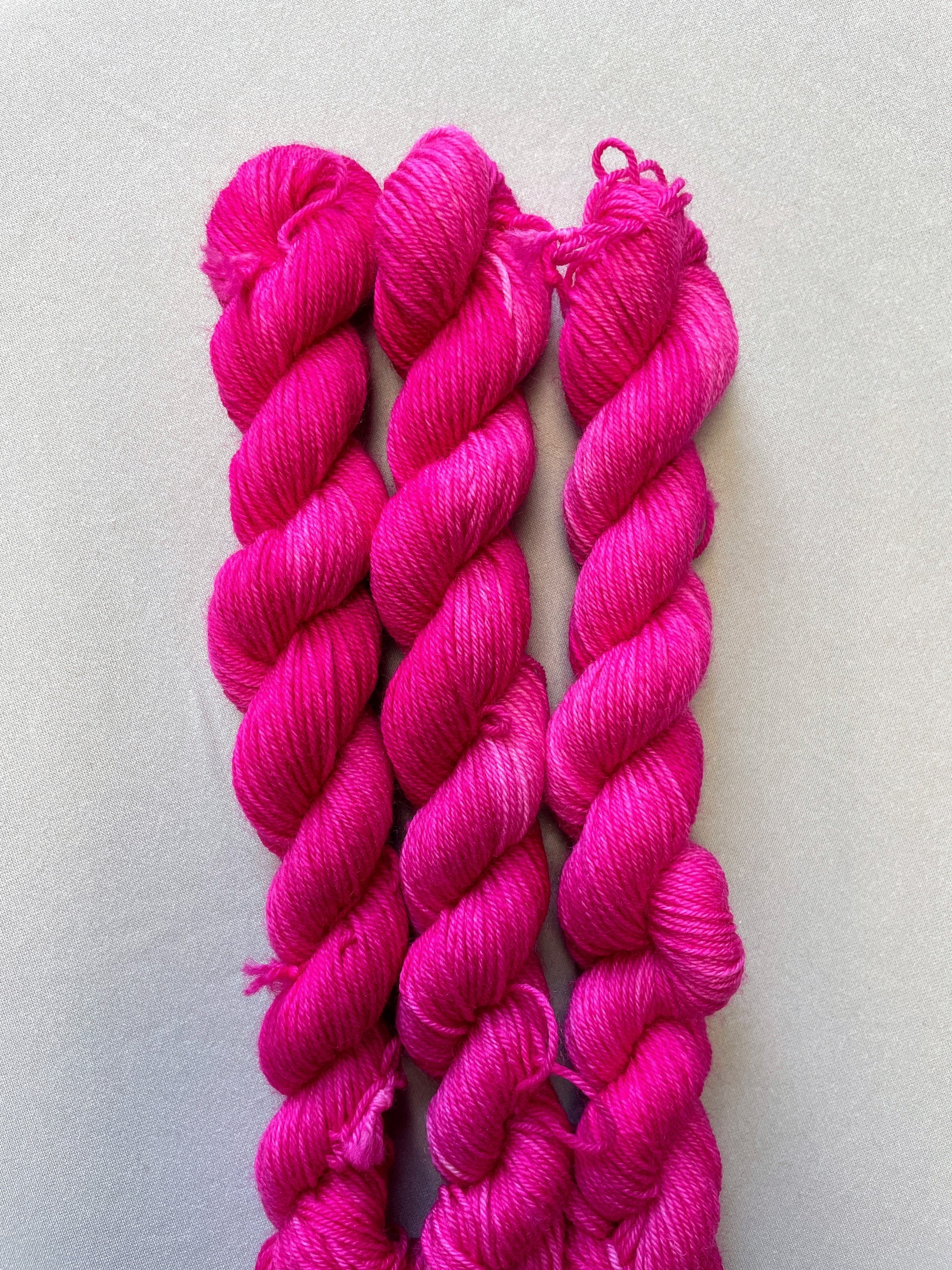 Close up shot of 20g sock weight mini skeins in colourway Pink. A semi-solid colourway in a bright pink shade.