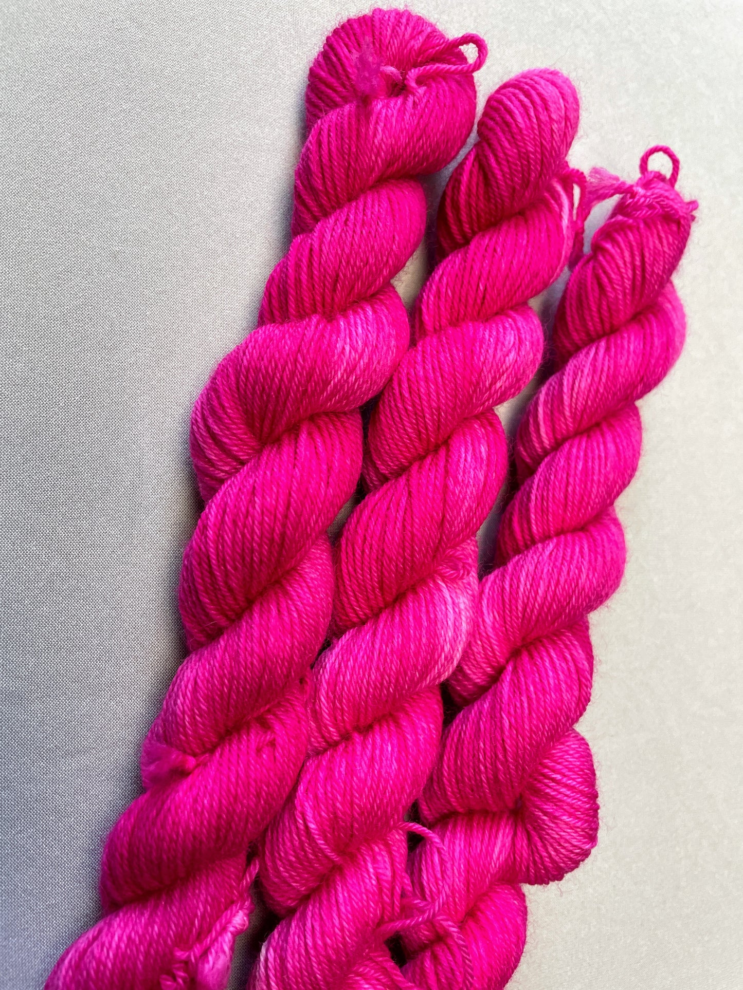 Close up shot of 20g sock weight mini skeins in colourway Pink. A semi-solid colourway in a bright pink shade.