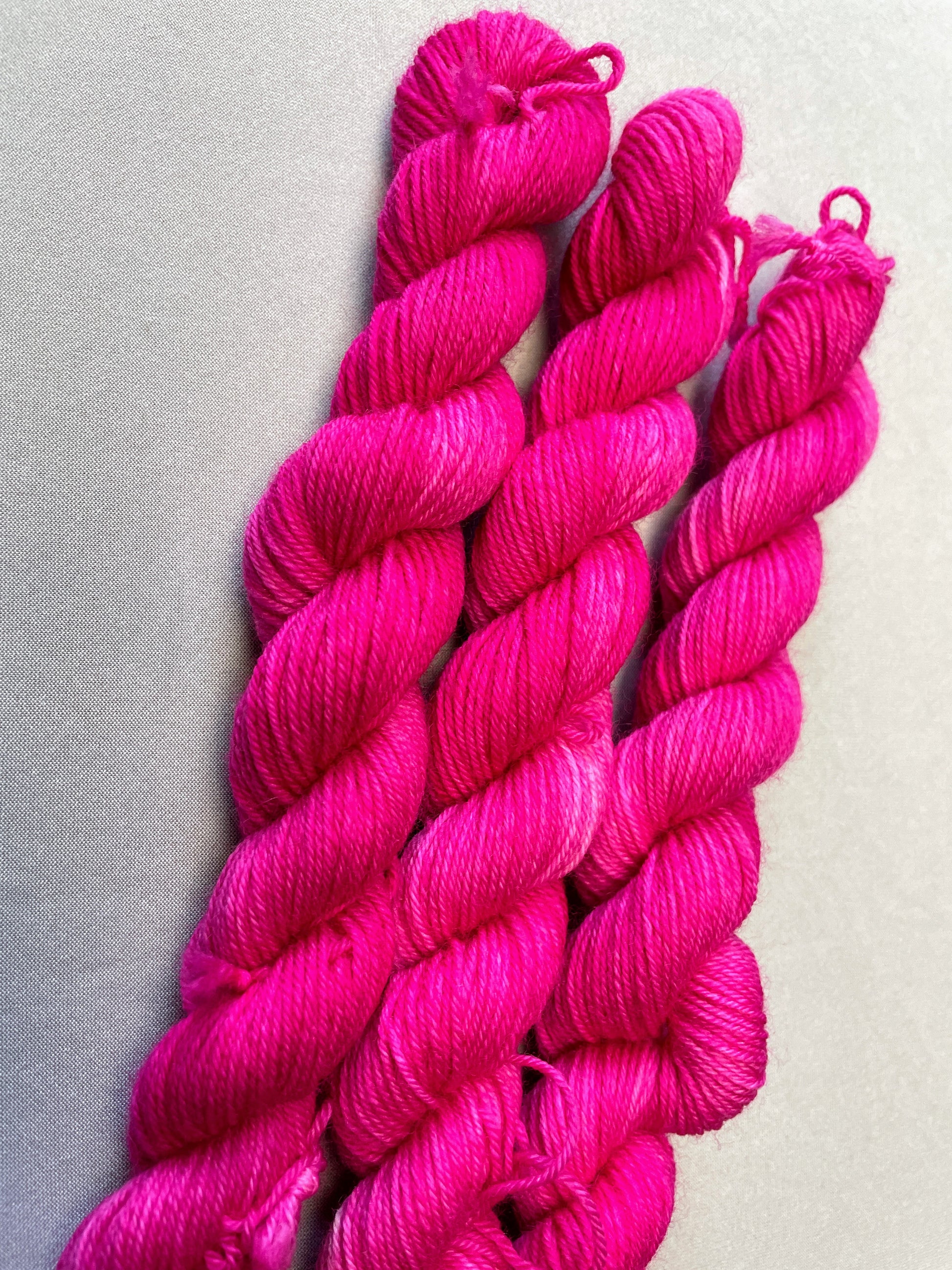 Close up shot of 20g sock weight mini skeins in colourway Pink. A semi-solid colourway in a bright pink shade.