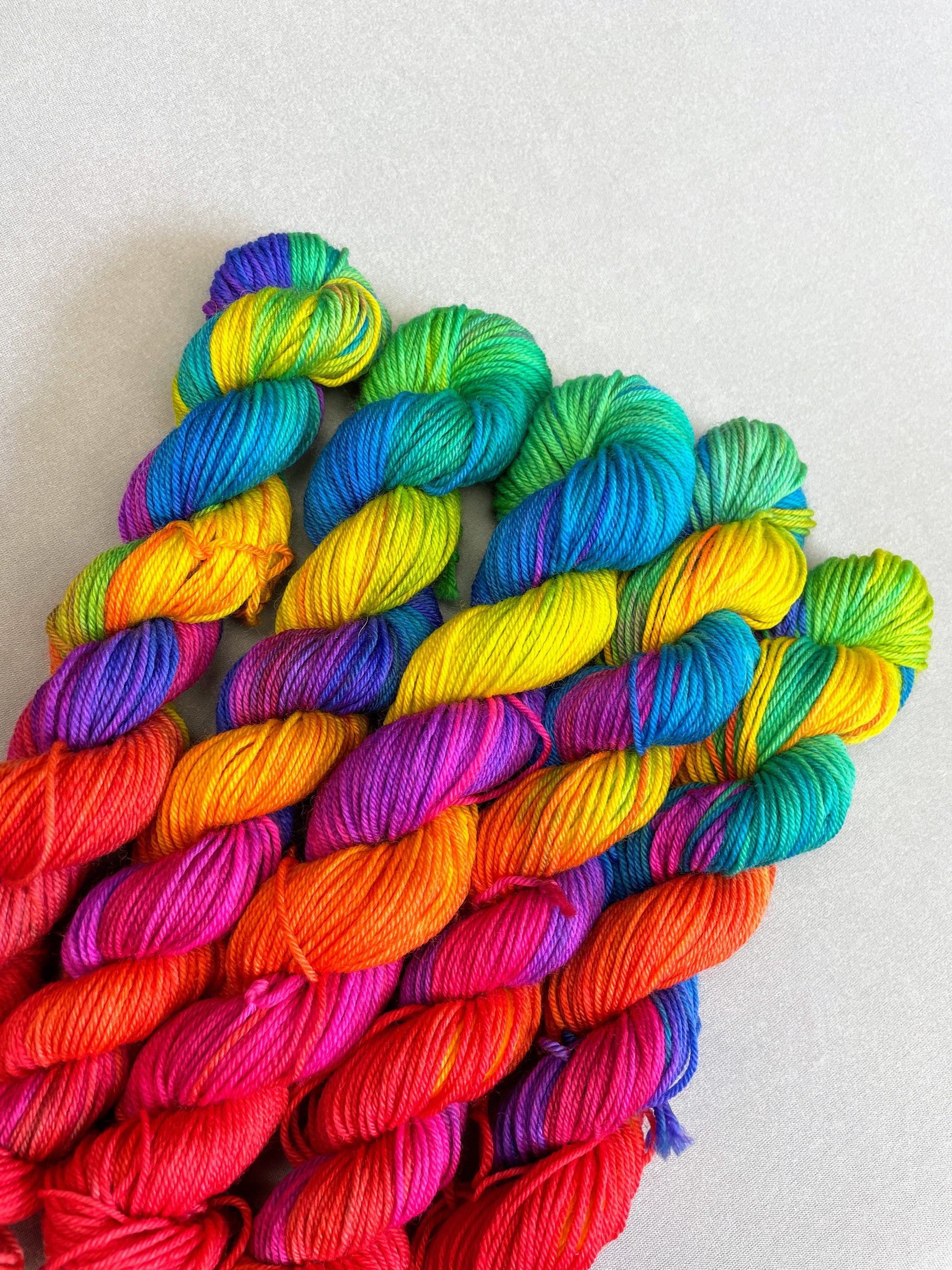 5 x 20g Hand-dyed Yarn mini skeins in colourway Bright Rainbow on our Sock/4ply Yarn base. The yarn contains 7 bright colours, sunshine, lava, ruby, apple, cyan, electric purple and neon pink and is photographed on a white background.
