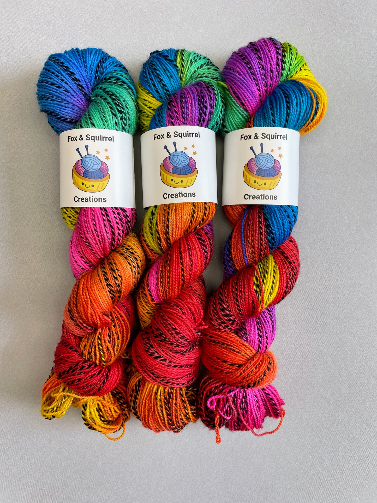 3 skeins of Hand-dyed Yarn in colourway Bright Rainbow on our Zebra Sock yarn base. The yarn contains 7 bright colours, sunshine, lava, ruby, apple, cyan, electric purple and neon pink and is photographed on a white background.