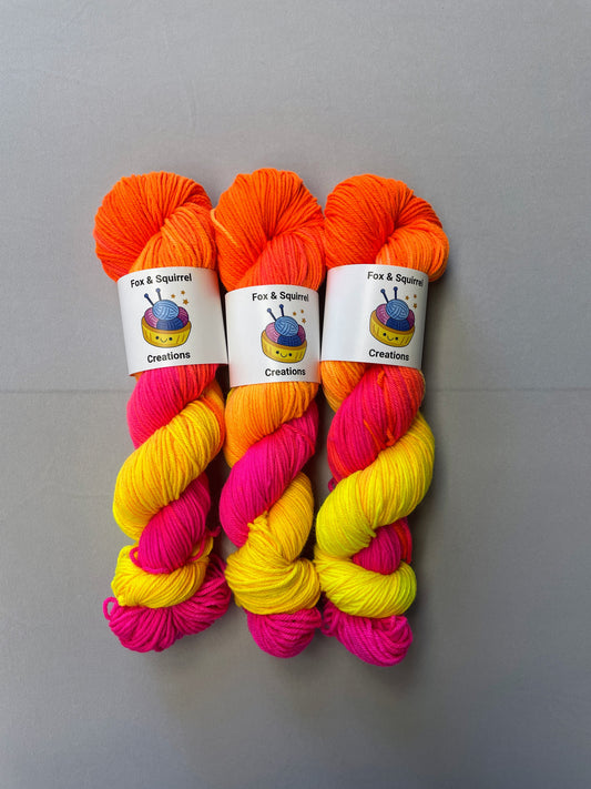 Full shot of 100g DK weight yarn in colourway Neon Funk. This colourway has three bands of colour in Neon Yellow, Neon Pink and Neon Orange. Photographed on a light grey background. 