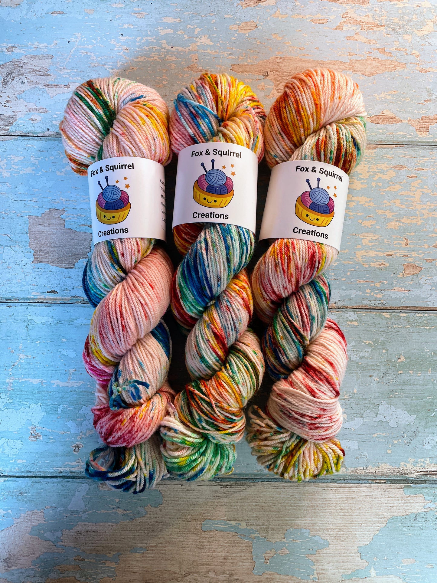 Full shot of 100g DK weight yarn in colourway Rainbow Sprinkles. This is an undeyd yarn base with layers of speckles in red, yellow, green, blue. 