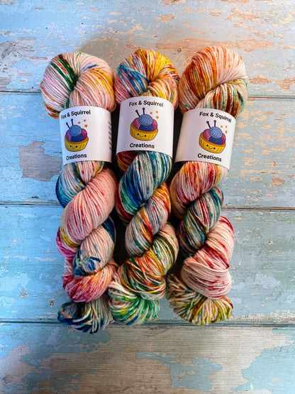 Full shot of 100g DK weight yarn in colourway Rainbow Sprinkles. This is an undeyd yarn base with layers of speckles in red, yellow, green, blue. 