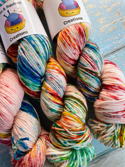 Close up shot of 100g DK weight yarn in colourway Rainbow Sprinkles. This is an undeyd yarn base with layers of speckles in red, yellow, green, blue. 