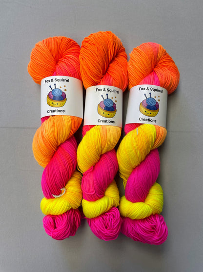 Zoomed in shot of 100g Sock weight yarn in colourway Neon Funk. This colourway has three bands of colour in Neon Yellow, Neon Pink and Neon Orange. Photographed on a light grey background. 