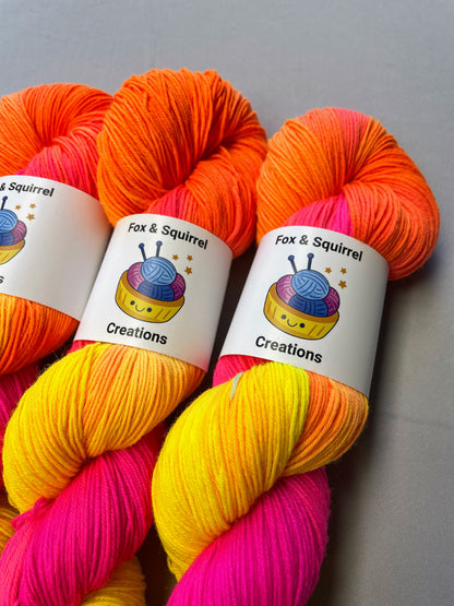 Full shot of 100g Sock weight yarn in colourway Neon Funk. This colourway has three bands of colour in Neon Yellow, Neon Pink and Neon Orange. Photographed on a light grey background. 