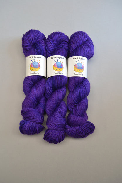 Full shot of 100g Sock weight yarn in semi-solid colourway Purple. This colourway is a deep and intense purple. Photographed on light grey background. 