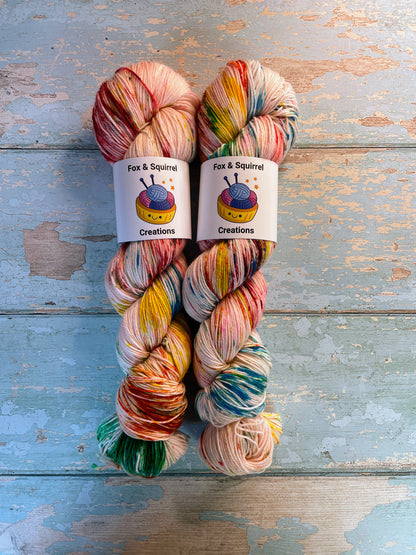 Full shot of 100g Sock weight yarn in colourway Rainbow Sprinkles. This is an undeyd yarn base with layers of speckles in red, yellow, green, blue. 