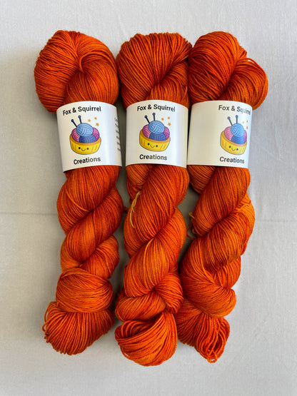 Close up shot of 100g sock weight skeins in semi-solid colourway, Saffron. A intense and deep Orange colourway.