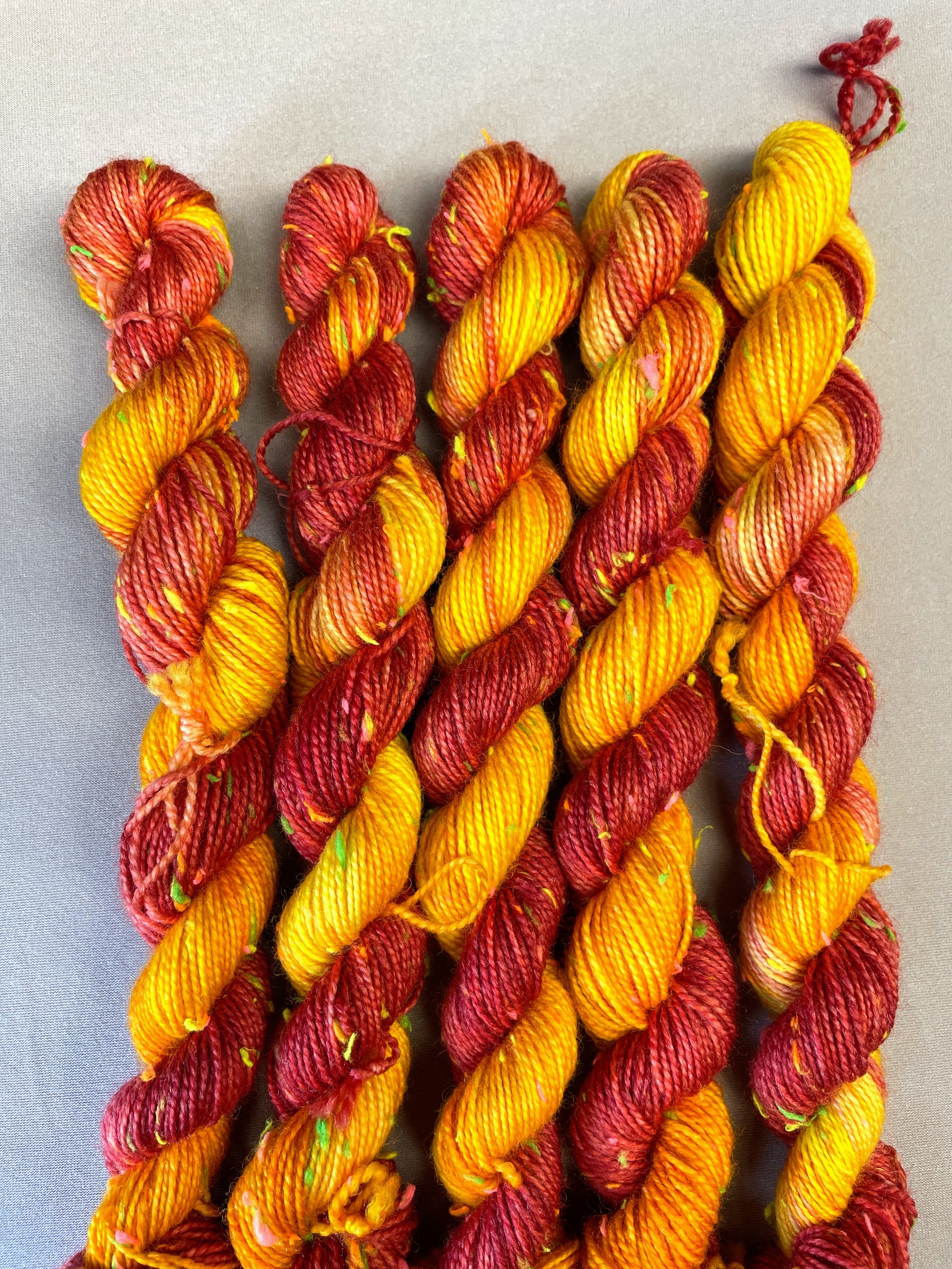 Hand-dyed Yarn
5 x 20g twisted, 4ply Neon Neps mini skeins in colourway Phoenix, photographed on light grey background. This colourway is full of tones of Golden Poppy, Ruby Red and Saffron with pops of Neon colour from the Neps.
