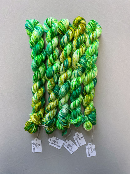 Full shot of 20g DK weight mini skeins in colourway Apple Sprinkles. Undyed yarn with layers of green speckles in tones Emerald, Olive Green and Neon Green. 