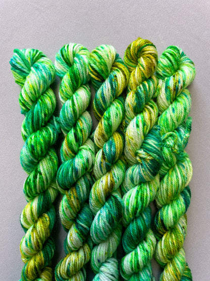 Close up shot of 20g DK weight mini skeins in colourway Apple Sprinkles. Undyed yarn with layers of green speckles in shades Emerald, Olive Green and Neon Green. 