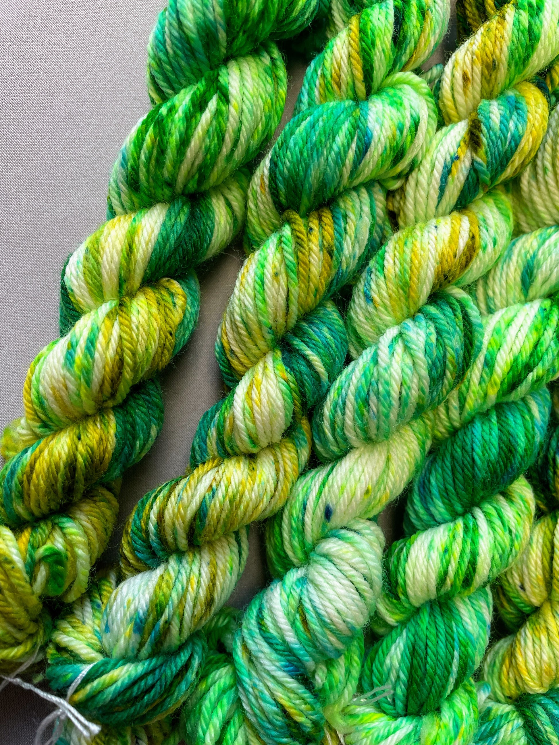 Zoomed in shot of 20g DK weight mini skeins in colourway Apple Sprinkles. Undyed yarn with layers of green speckles in shades Emerald, Olive Green and Neon Green. 