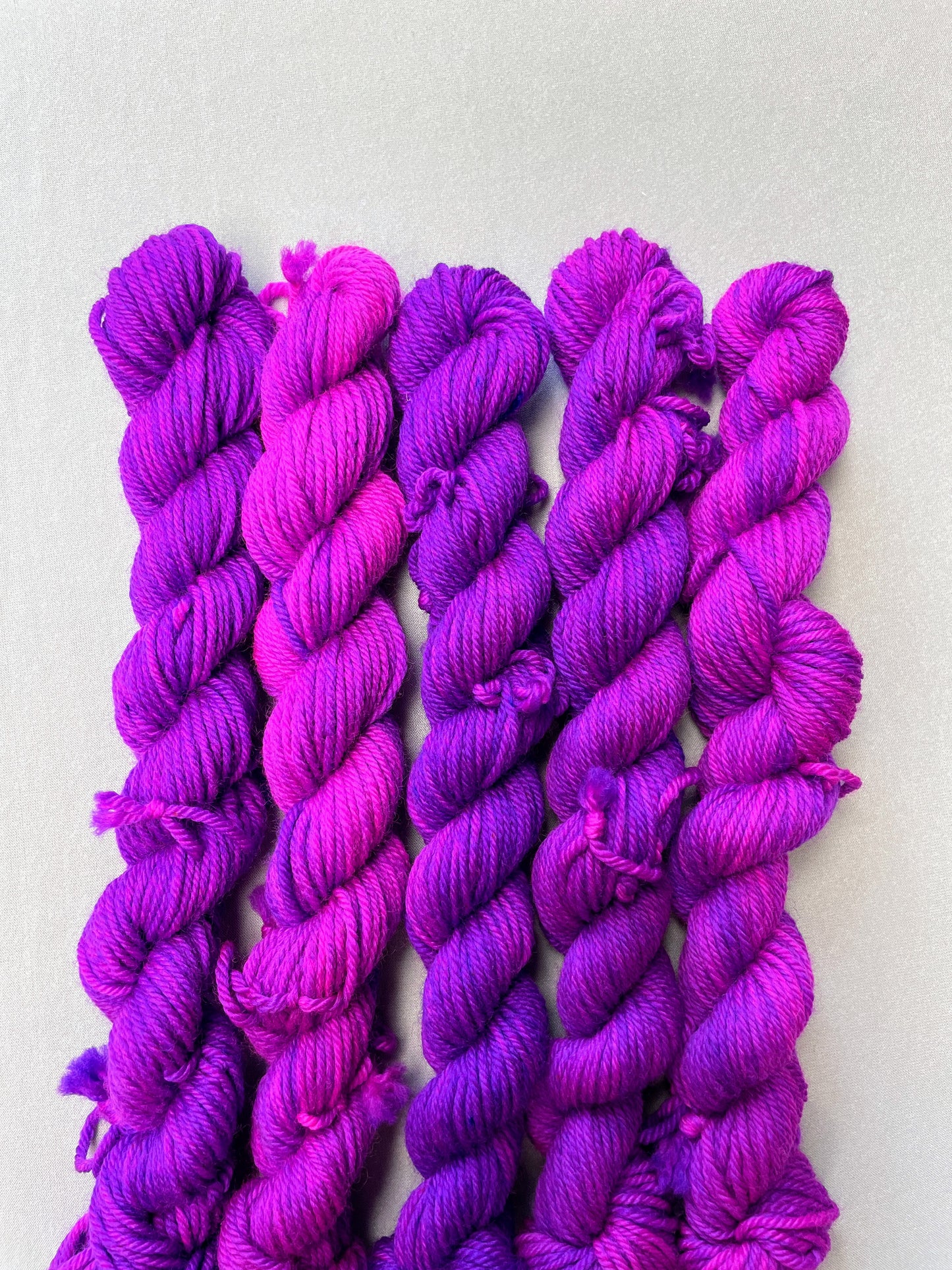 Zoomed in shot of 20g DK weigh mini skeins in colourway Electric Purple. This colourway is an intense and bright purple that breaks into Neon Pink. Photographed on light grey background.