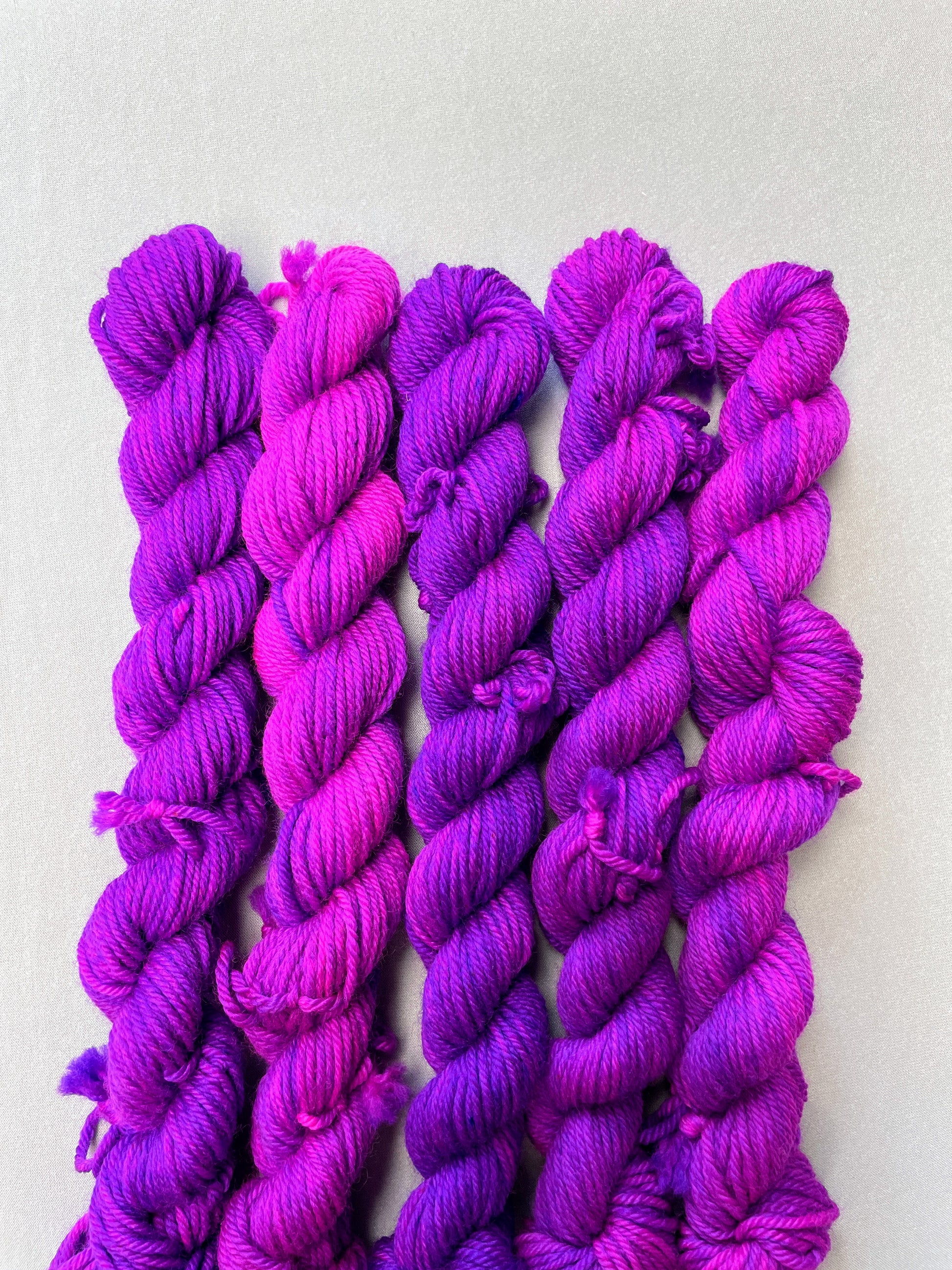 Zoomed in shot of 20g DK weigh mini skeins in colourway Electric Purple. This colourway is an intense and bright purple that breaks into Neon Pink. Photographed on light grey background.