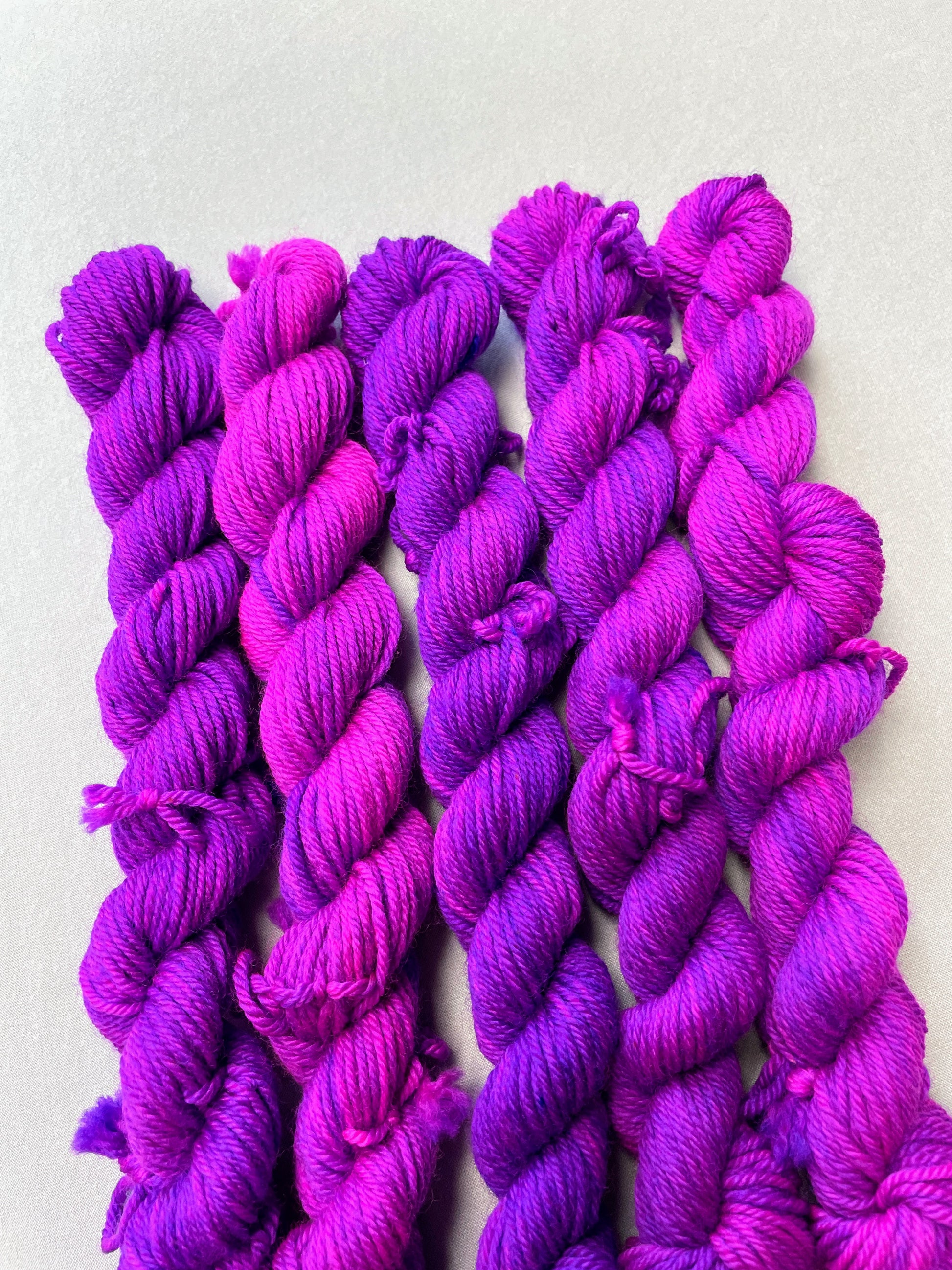 Close up shot of 20g DK weigh mini skeins in colourway Electric Purple. This colourway is an intense and bright purple that breaks into Neon Pink. Photographed on light grey background.