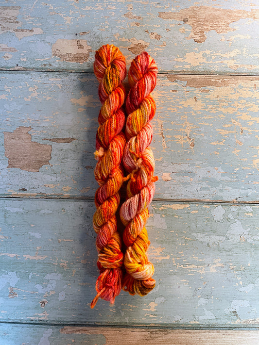 Full shot of 20g DK weight mini skeins in colourway Fire Sprinkles. Undyed yarn with layers of dye speckles in shades, Orange, Red and Mustard. 