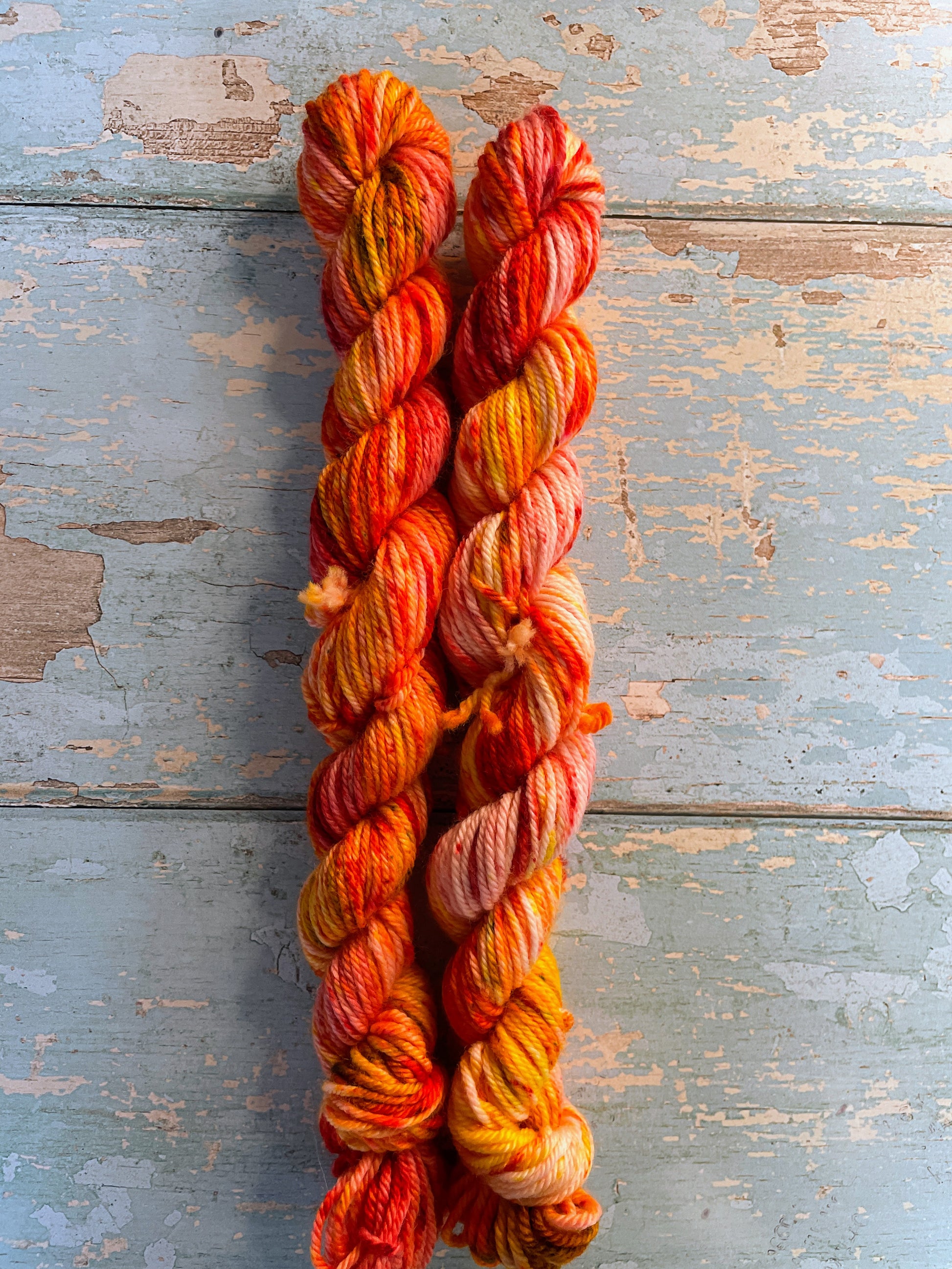 Zoomed in shot of 20g DK weight mini skeins in colourway Fire Sprinkles. Undyed yarn with layers of dye speckles in shades, Orange, Red and Mustard. 