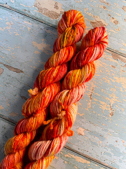 Close up shot of 20g DK weight mini skeins in colourway Fire Sprinkles. Undyed yarn with layers of dye speckles in shades, Orange, Red and Mustard. 