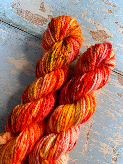 Close up shot of 20g DK weight mini skeins in colourway Fire Sprinkles. Undyed yarn with layers of dye speckles in shades, Orange, Red and Mustard. 